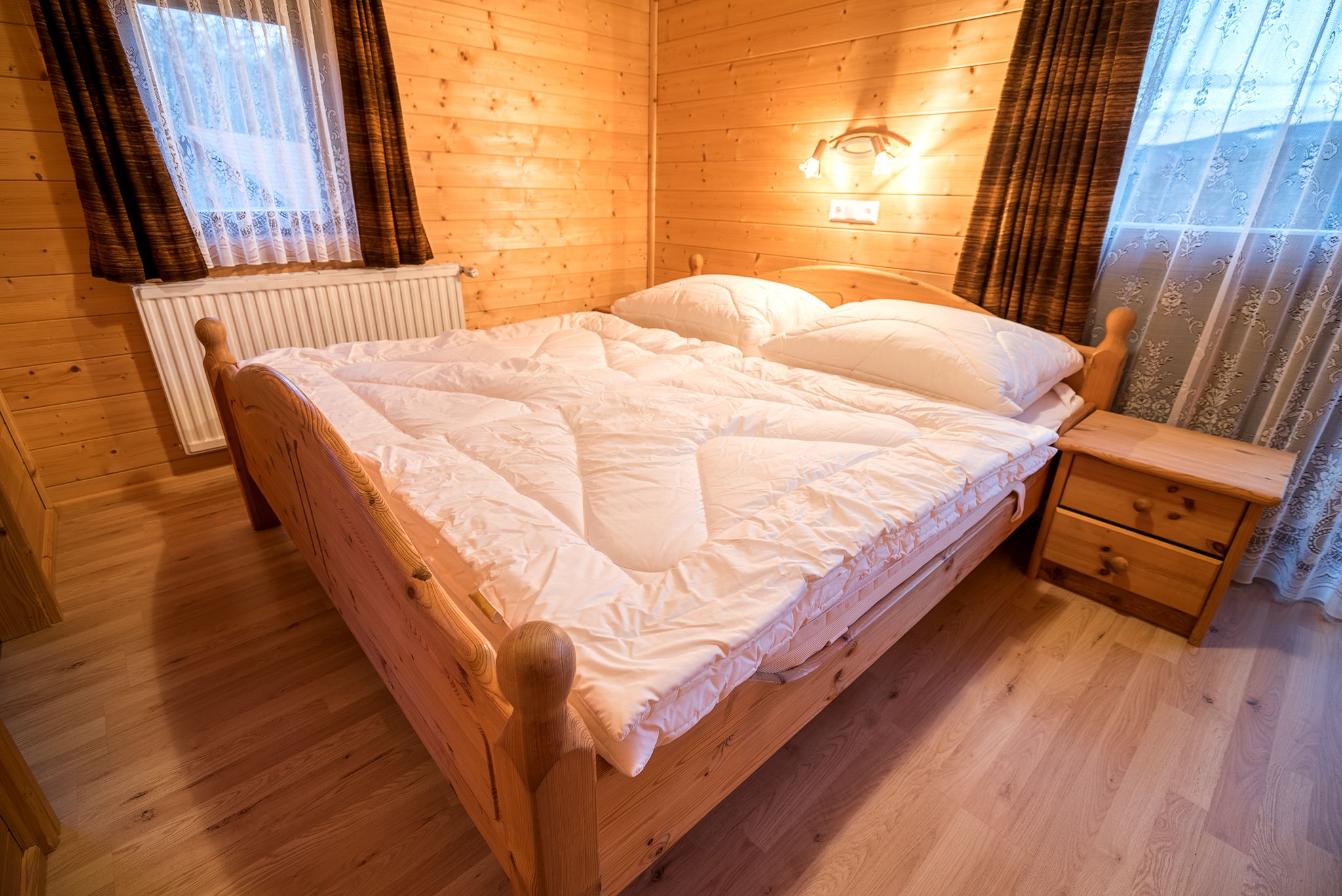 Hangulatos hálószoba fából készült falakkal, franciaággyal és éjjeliszekrénnyel egy nyaraló apartmanban.