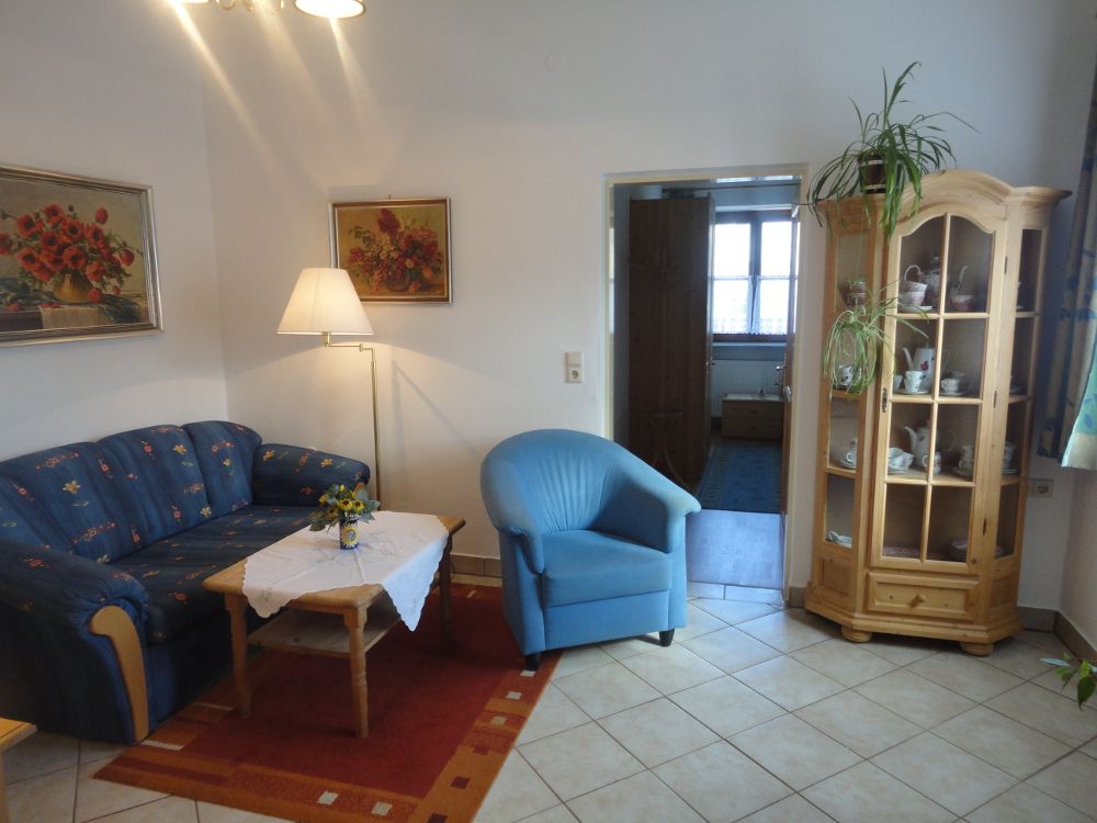 Nappali kék kanapéval, kék karosszékkel, fa asztallal és vitrinnel.