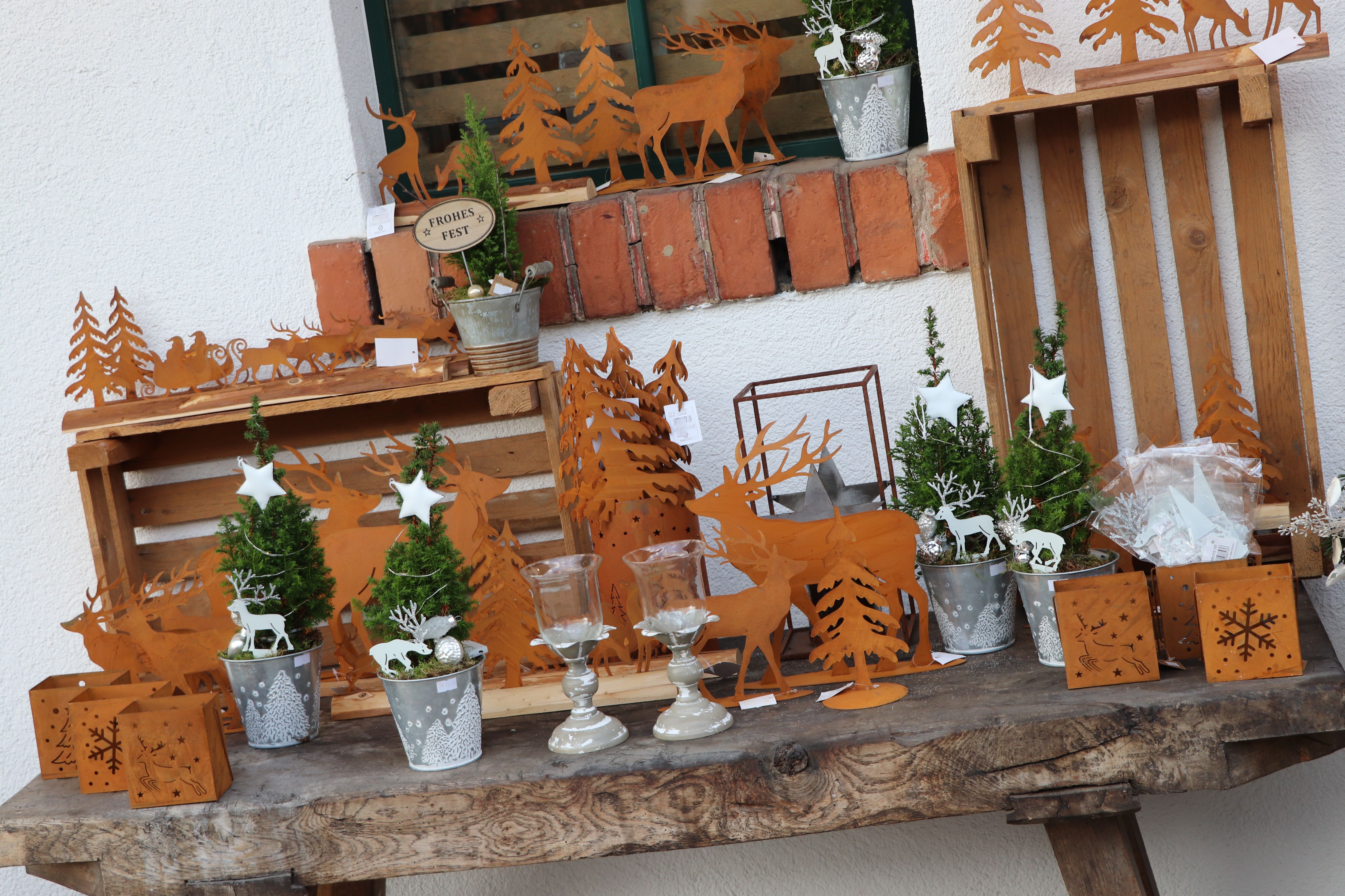 Karácsonyi dekoráció fém rénszarvas és karácsonyfa motívumokkal egy fa asztalon.