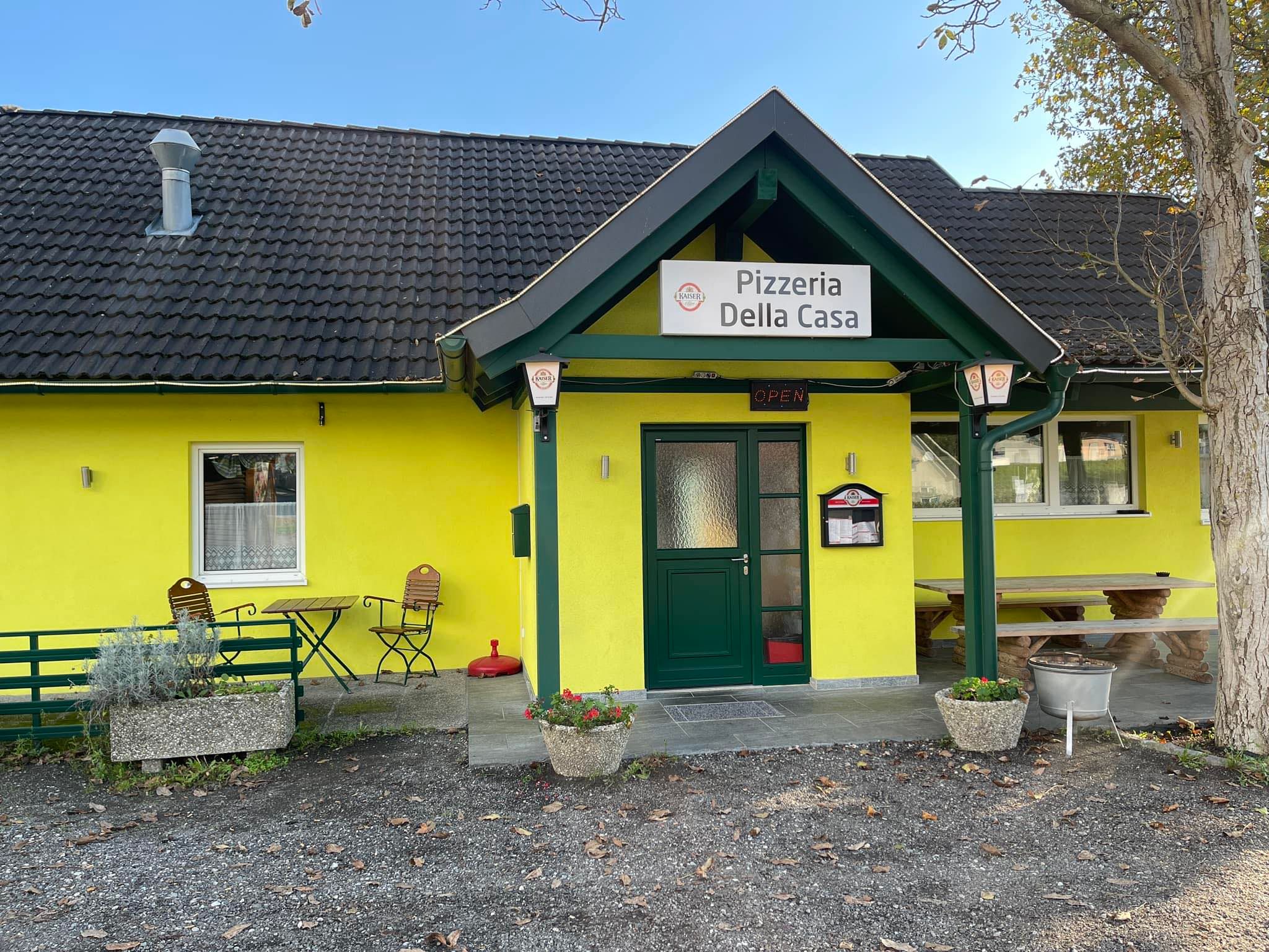 Egy sárga színű pizzéria külső nézete a "Pizzeria Della Casa" felirattal.