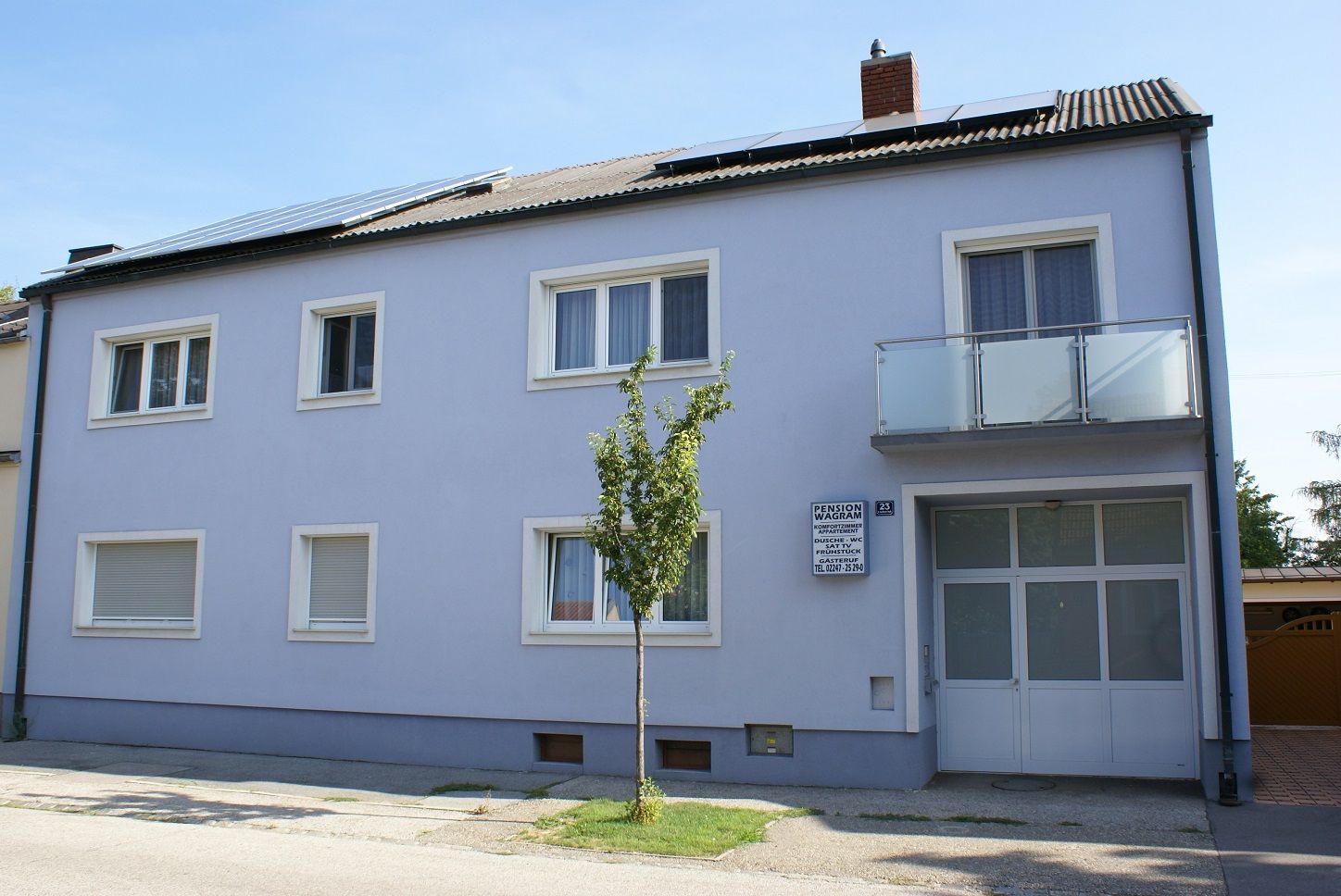 Egy kétszintes épület külső nézete, kék homlokzattal és napelemekkel a tetőn.