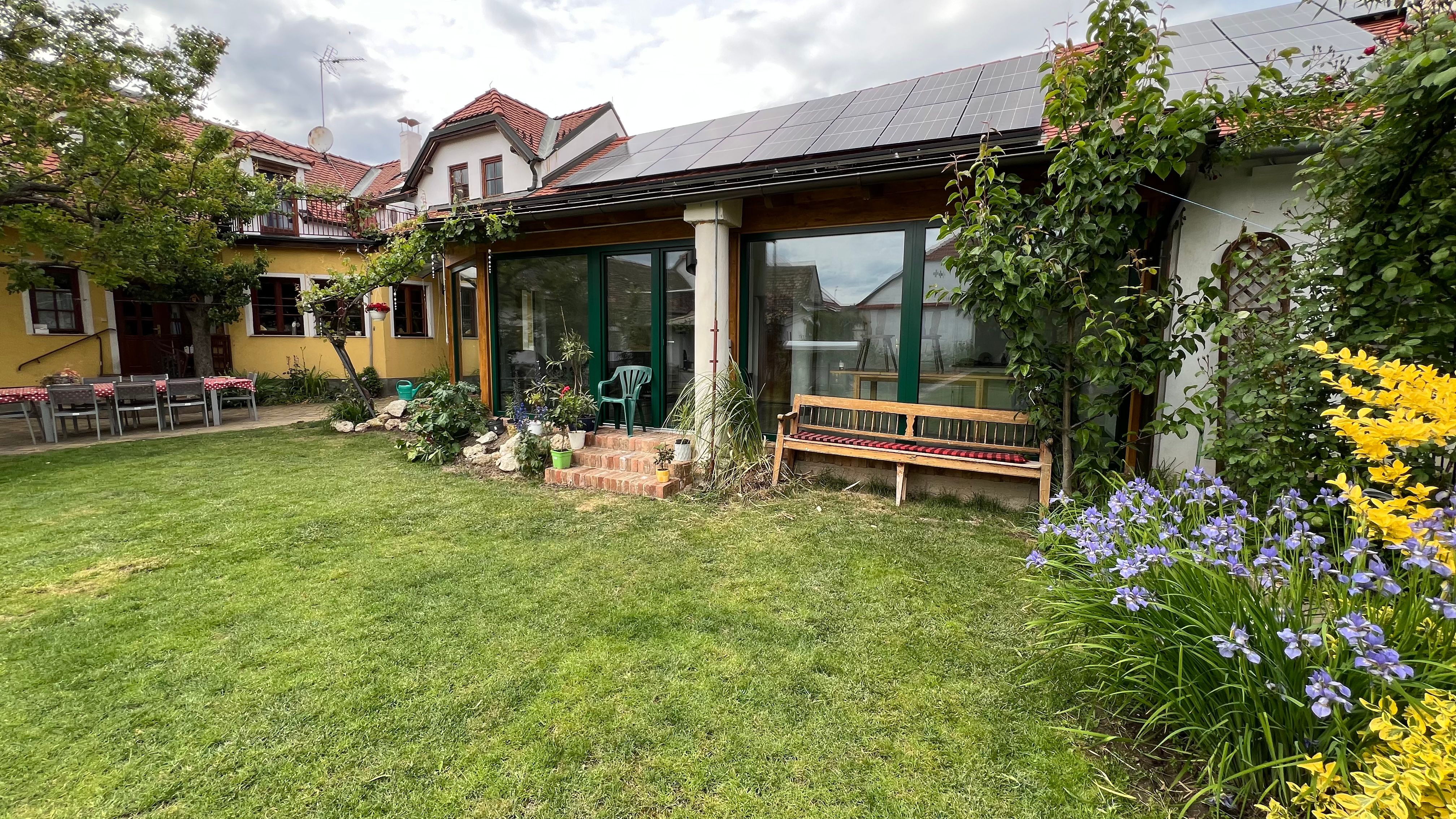 Kert pázsittal, virágágyásokkal és egy napelemes házzal a tetőn.