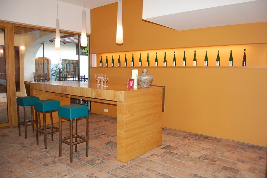 Modern kóstolóterem fapultokkal, bárszékekkel és borosüvegekkel a falon.