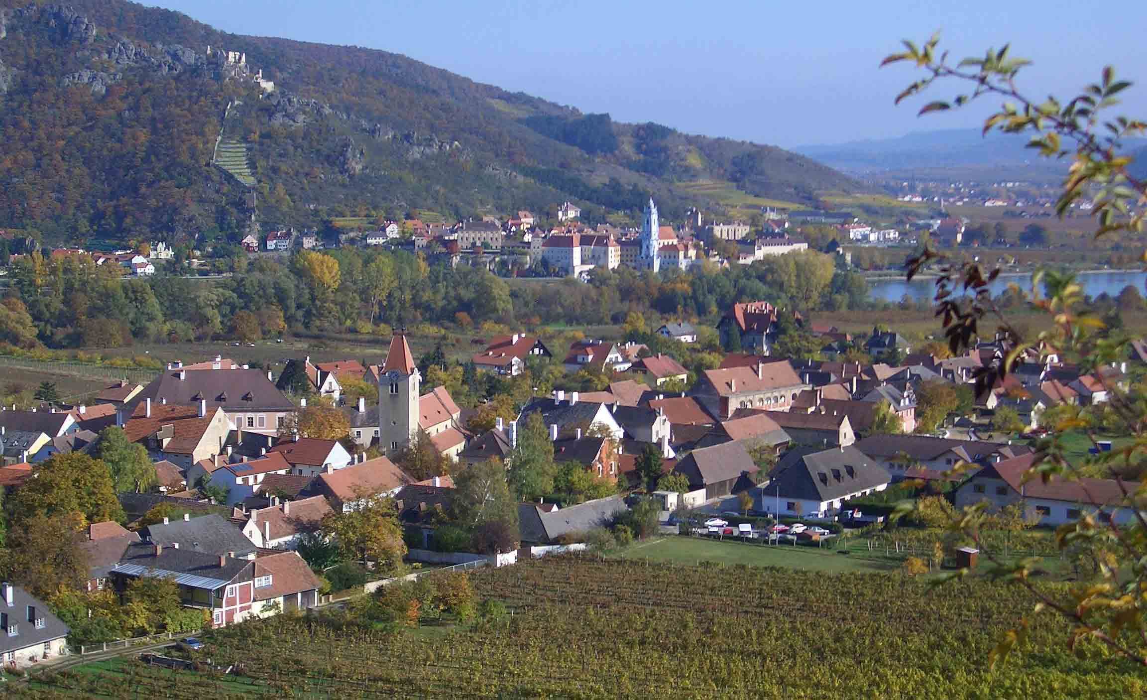 Panoráma egy festői városról, a háttérben szőlőültetvényekkel és folyóval.