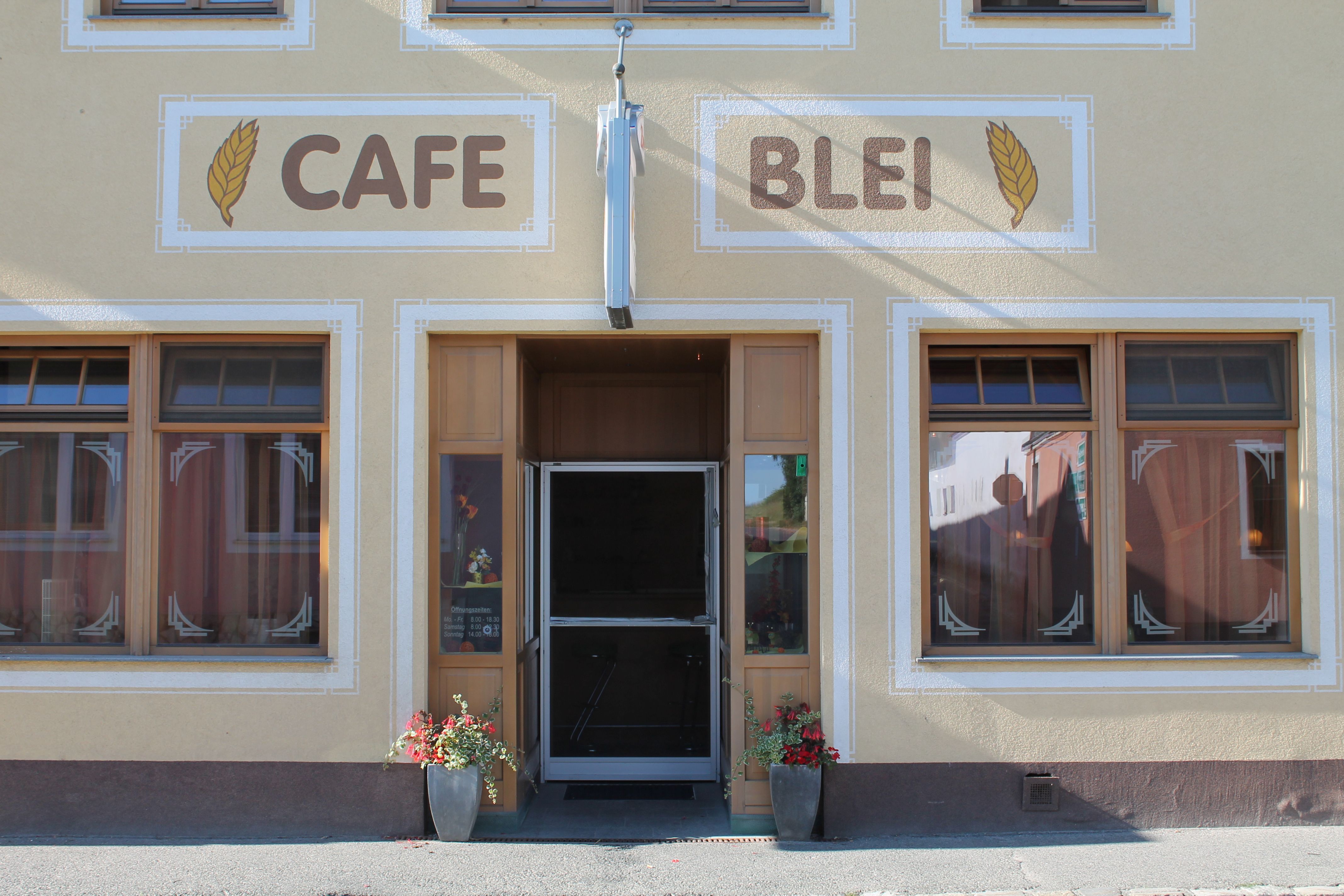 Egy kávézó bejárata "Cafe Blei" felirattal és virágos díszítéssel.