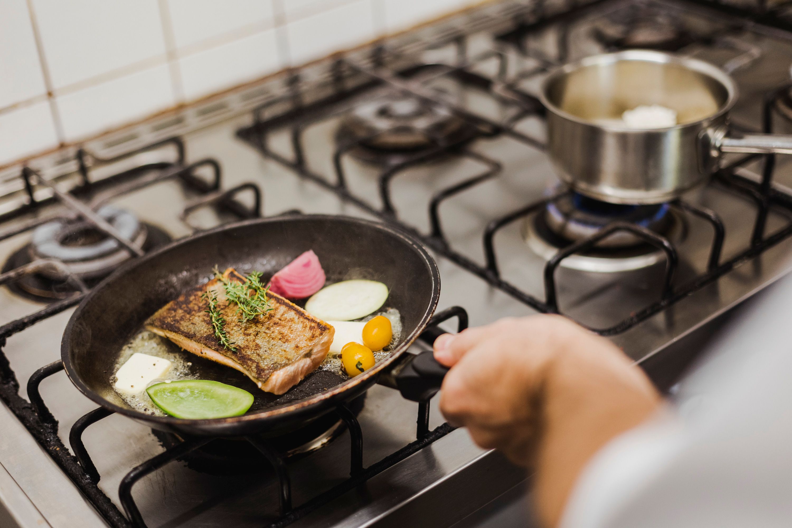 Egy serpenyő halakkal, zöldségekkel és fűszernövényekkel a főzőlapon.