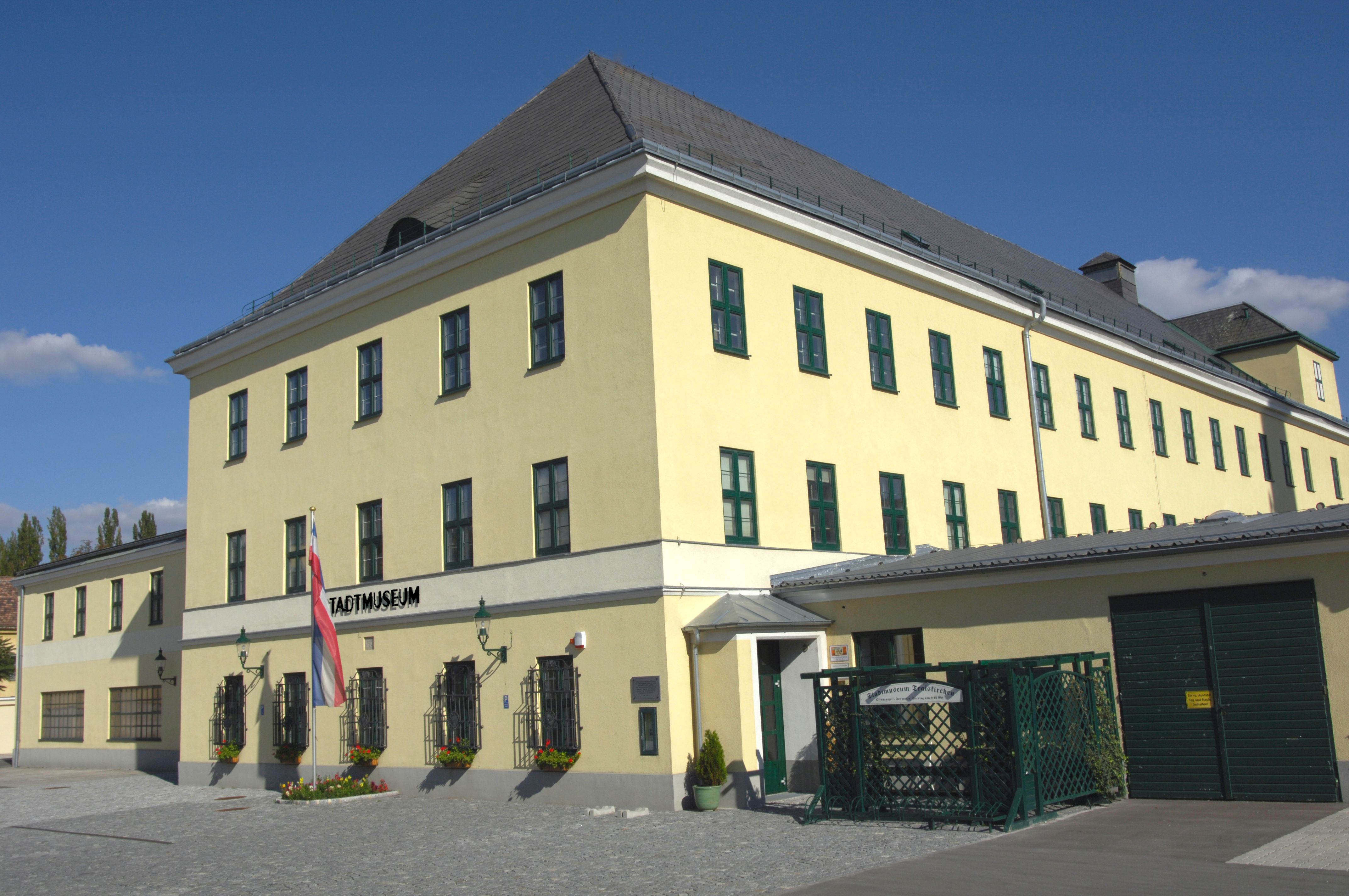 Sárga épület "Stadtmuseum" felirattal és egy osztrák zászlóval előtte.