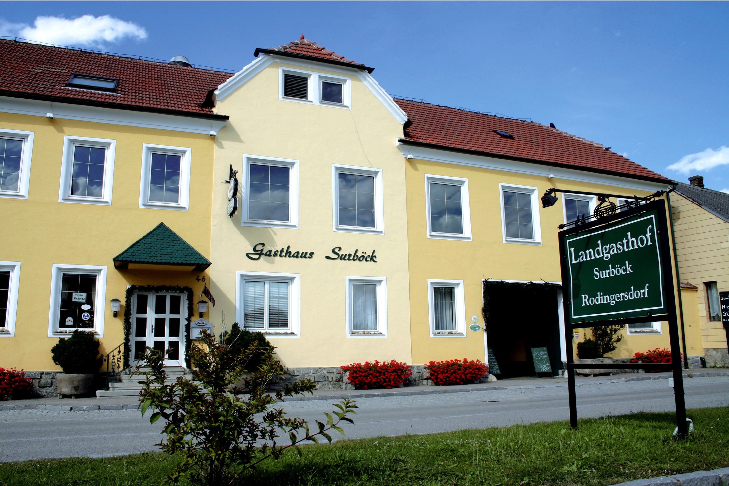 Sárga épület "Gasthaus Surböck" felirattal és zöld felirattal "Landgasthof Surböck Rodingersdorf".