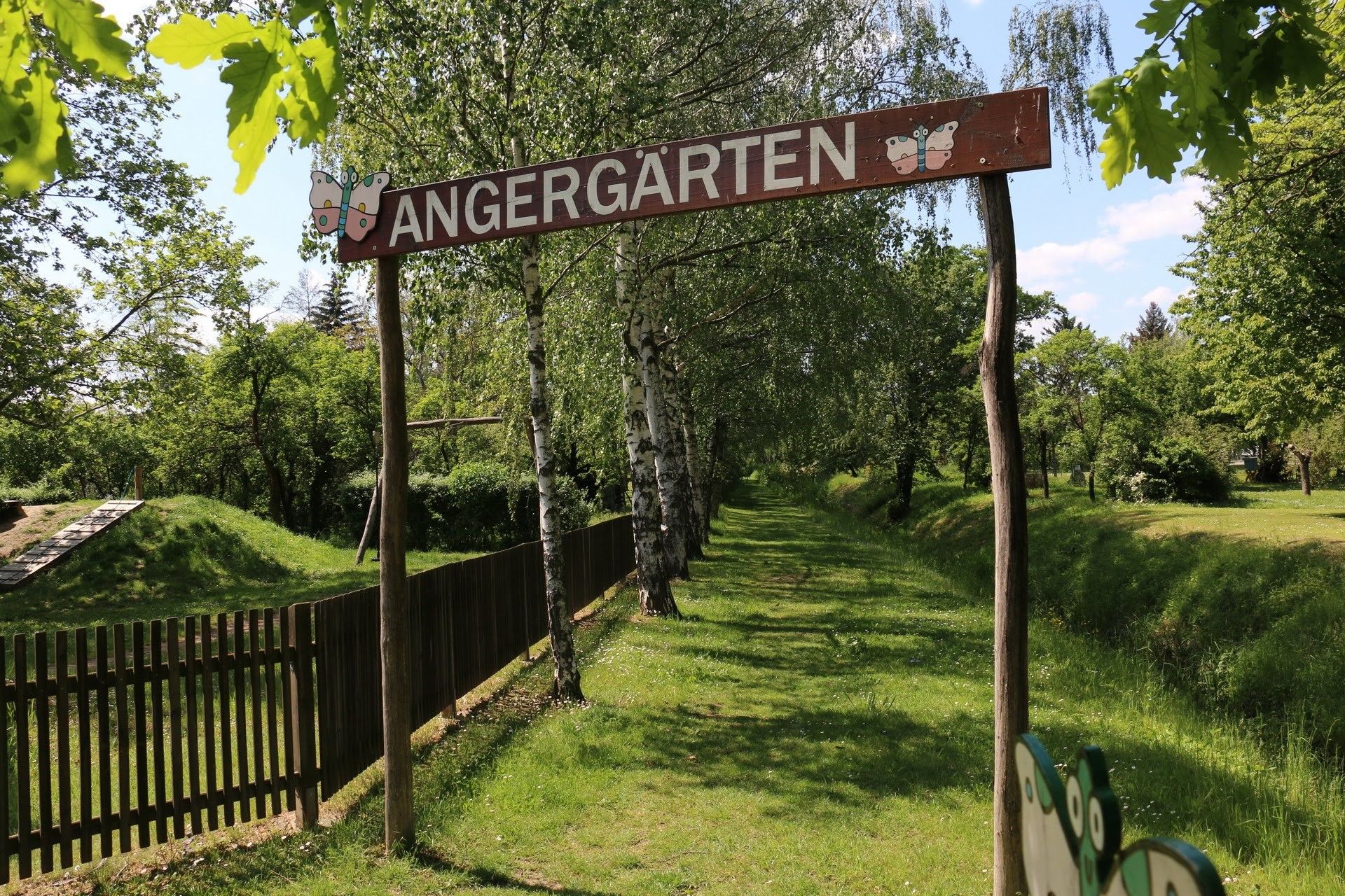 Az Angergärten bejárata fából készült táblával és fákkal a háttérben.