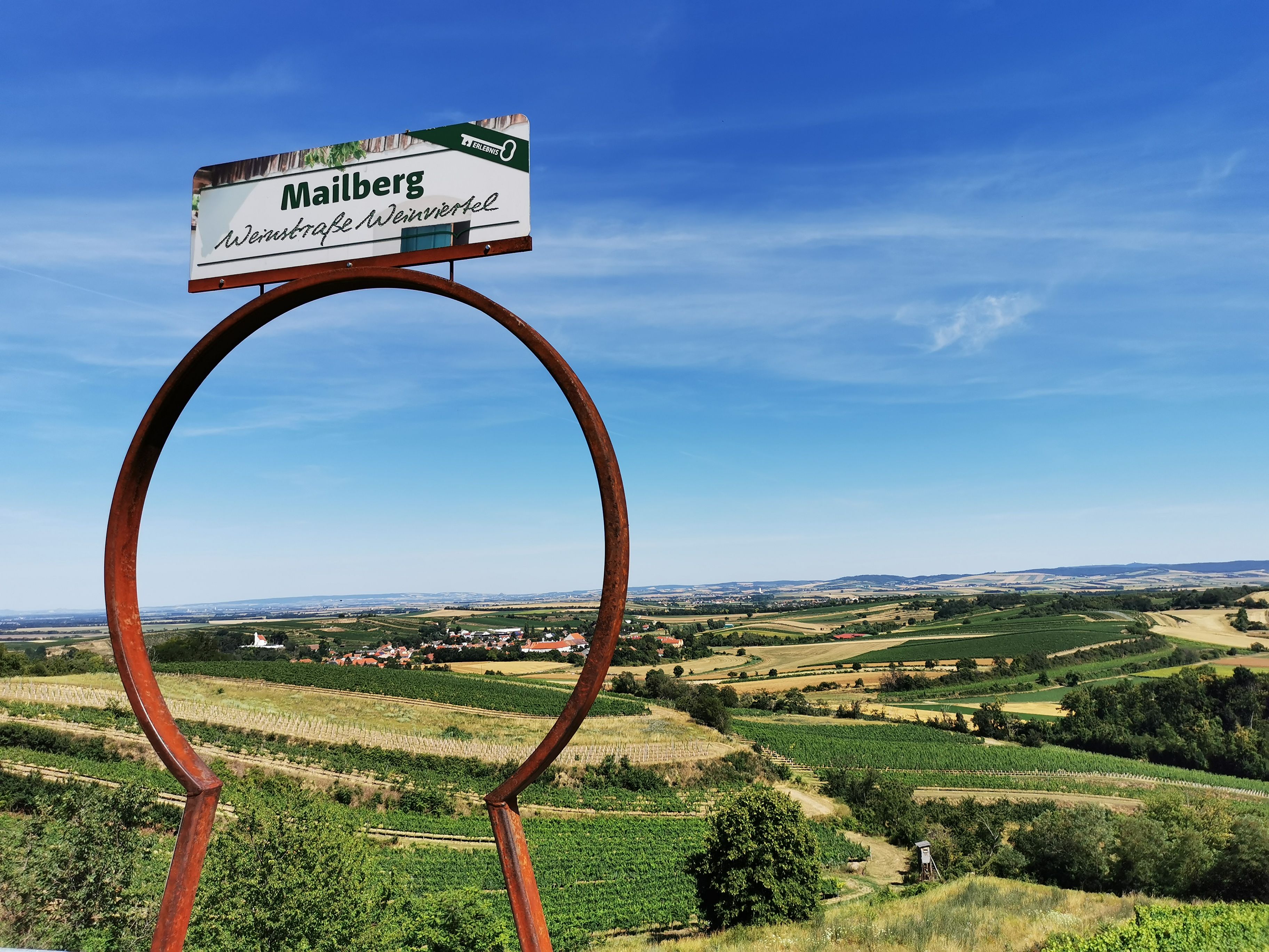 Tájkép szőlőültetvényekkel és "Mailberg Borút Weinviertel" feliratú táblával.