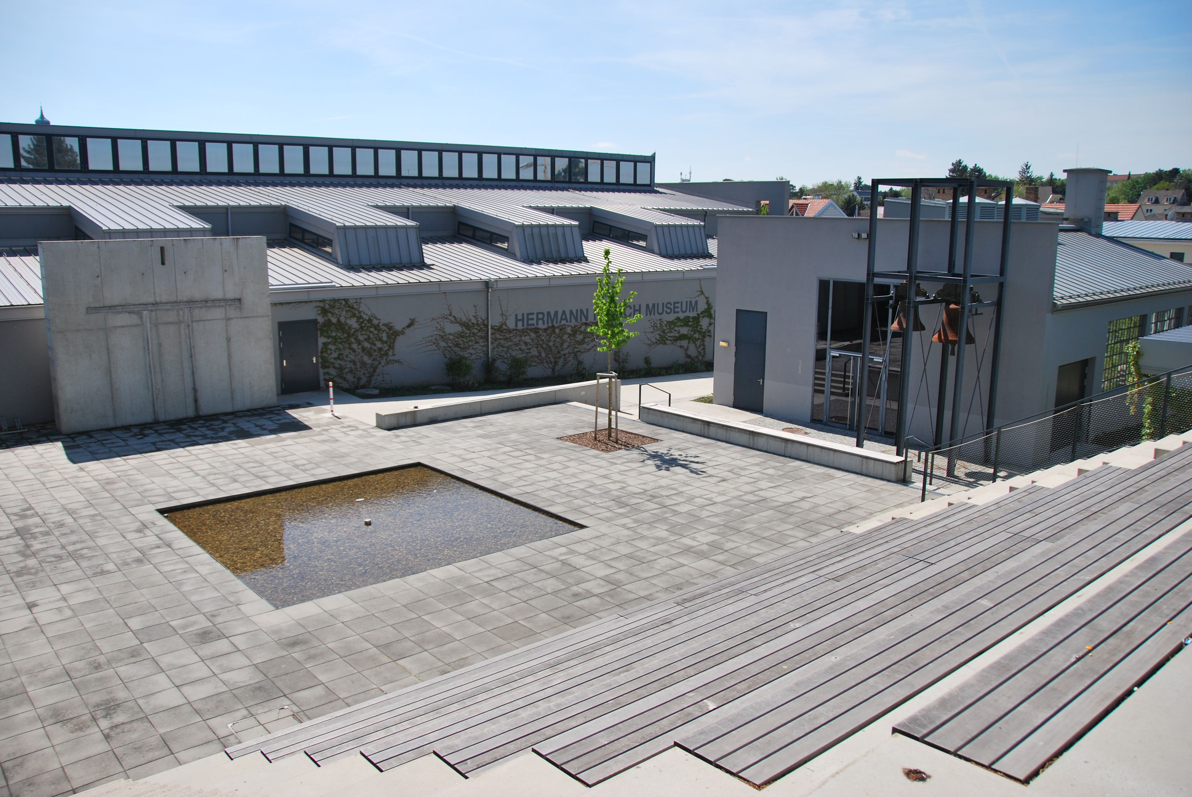 A Hermann Nitsch Múzeum külső nézete modern dizájnnal és egy kis vízmedencével a téren.