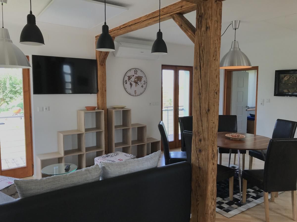 Modern nappali fagerendákkal, étkezőasztallal, székekkel, fali polccal, órával és TV-vel.