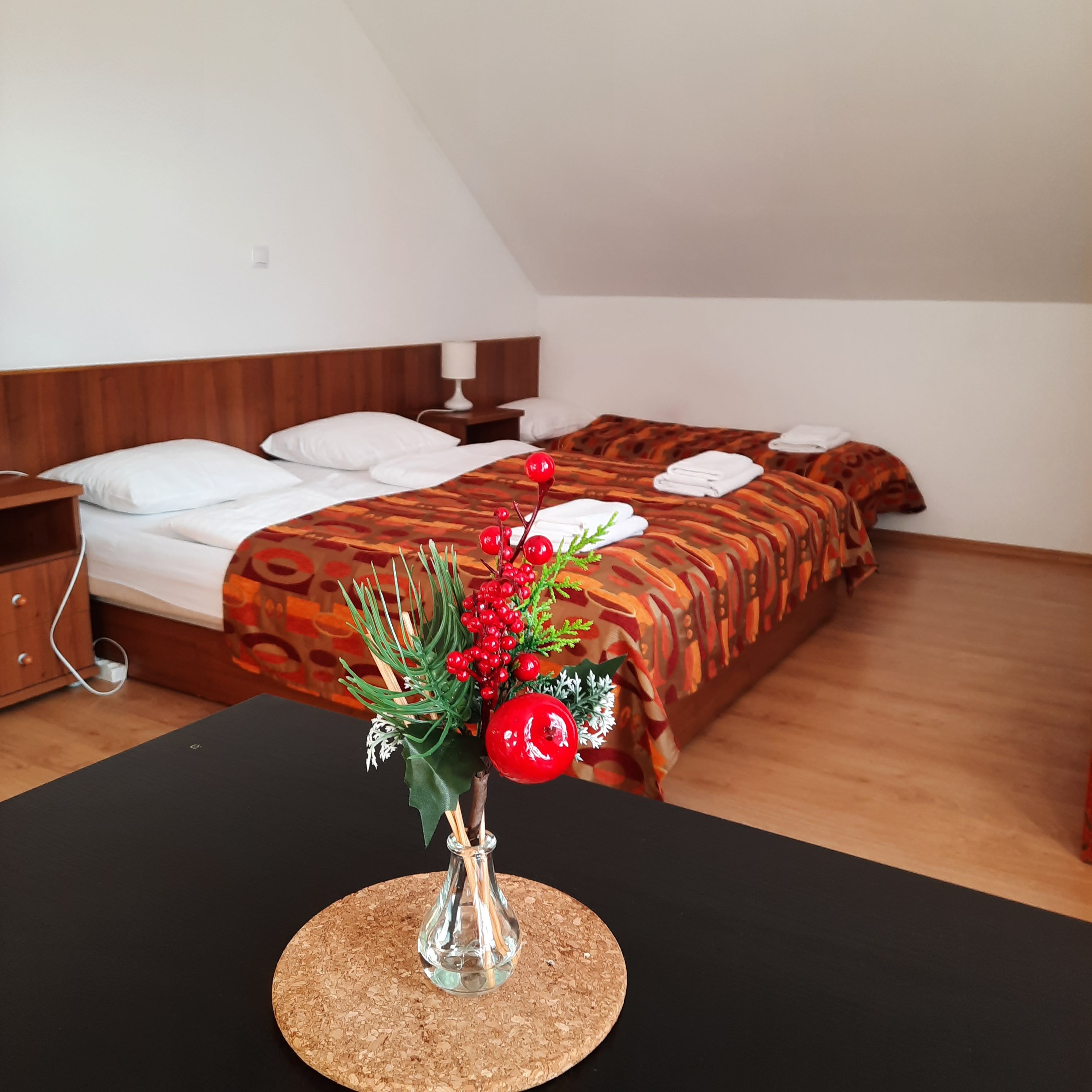 Hangulatos hálószoba két ággyal, az előtérben vörös bogyókkal díszített vázában.