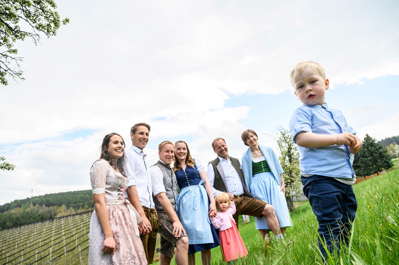 Egy hagyományos öltözetű család áll a réten, előtérben egy kisfiú.