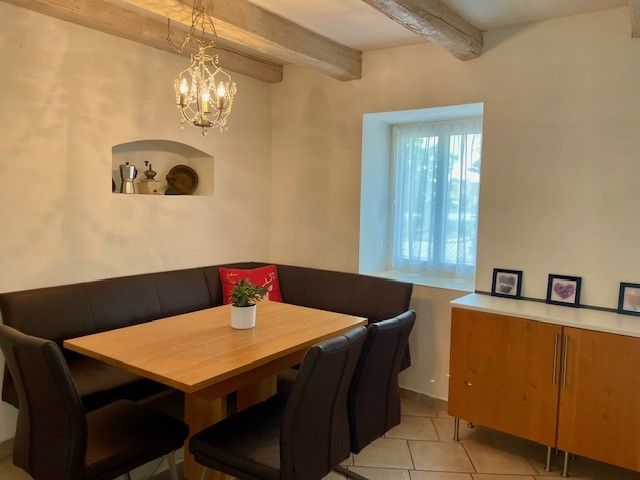 Hangulatos étkező, fa asztallal, fekete székekkel és sarokpaddal. A falon csillár lóg, mellette egy ablak és egy komód.