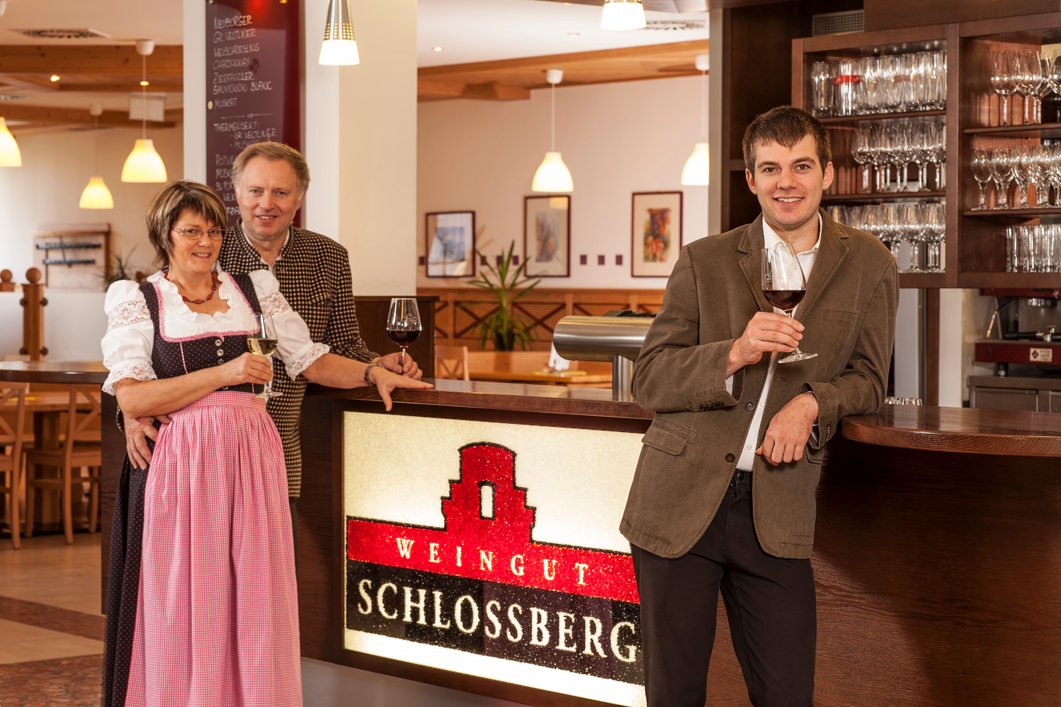 Három ember áll a Schlossberg pincészet pultjánál, kezükben pohár borral.