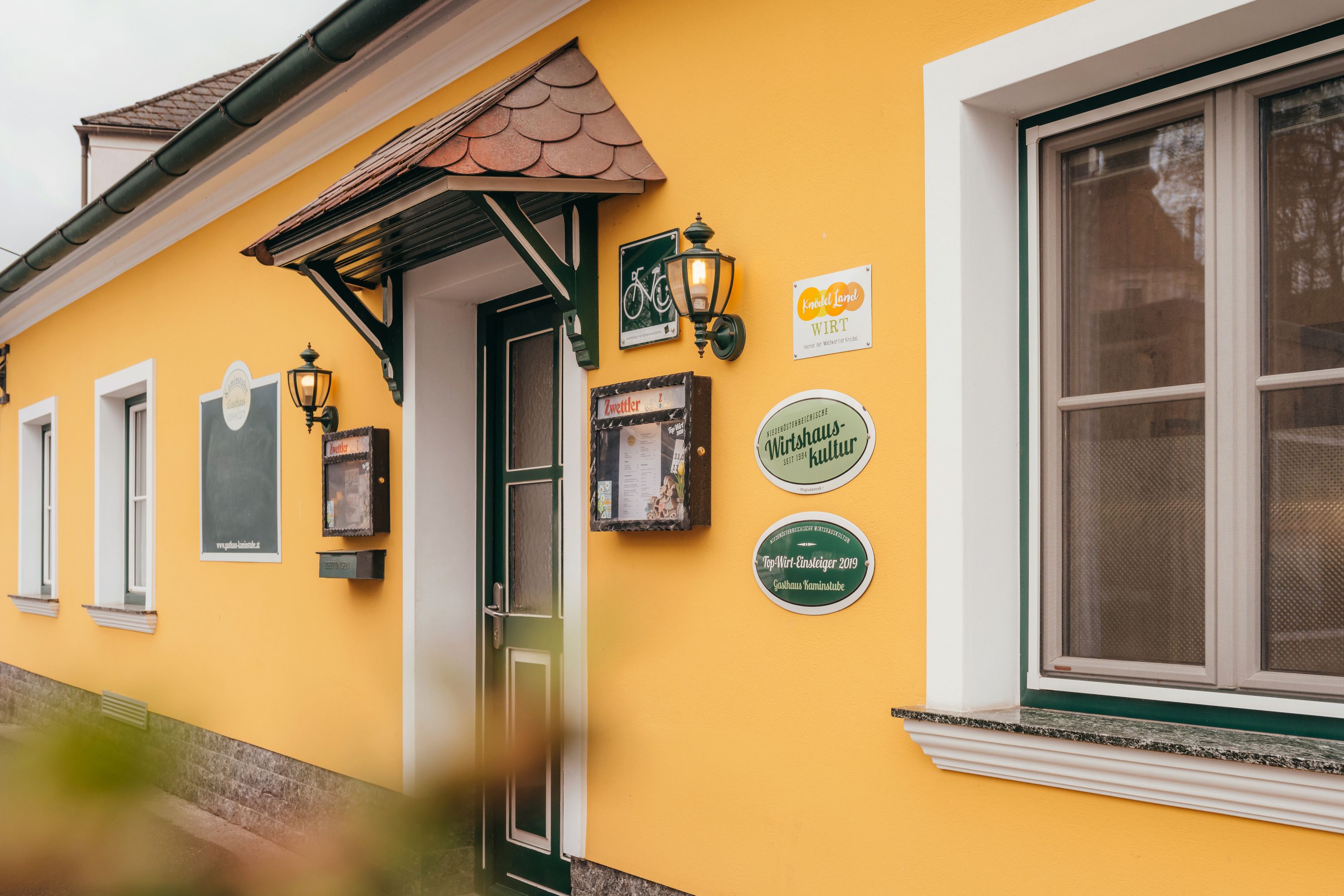 Sárga épület ajtóval és ablakokkal, táblákkal és lámpákkal a falon.