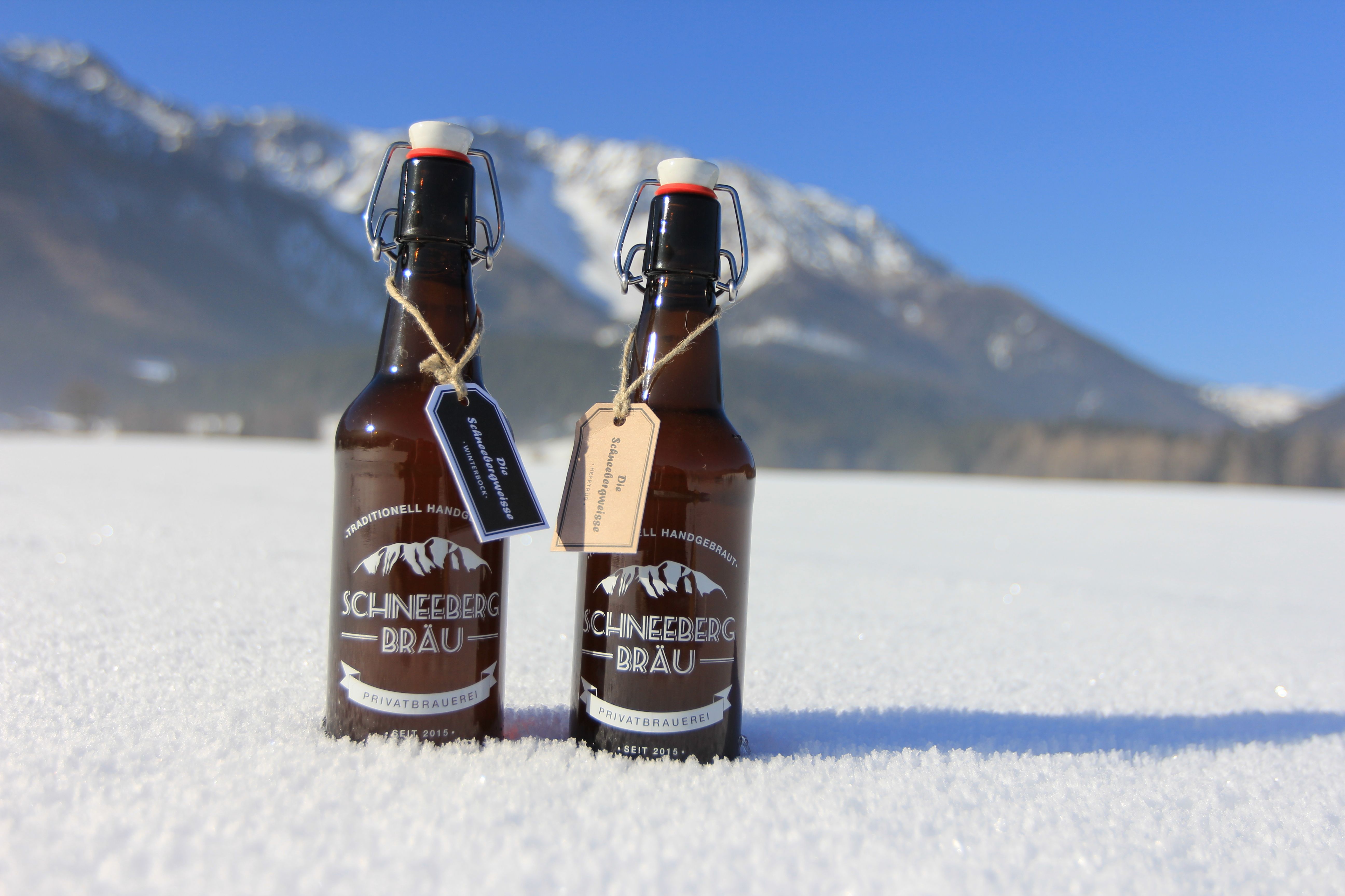Két üveg Schneeberg Bräu sör áll a hóban a hegyi háttér előtt.