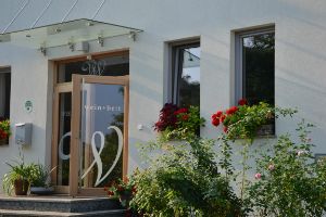 Egy "wein + bett" feliratú épület bejárata, virágokkal körülvéve.