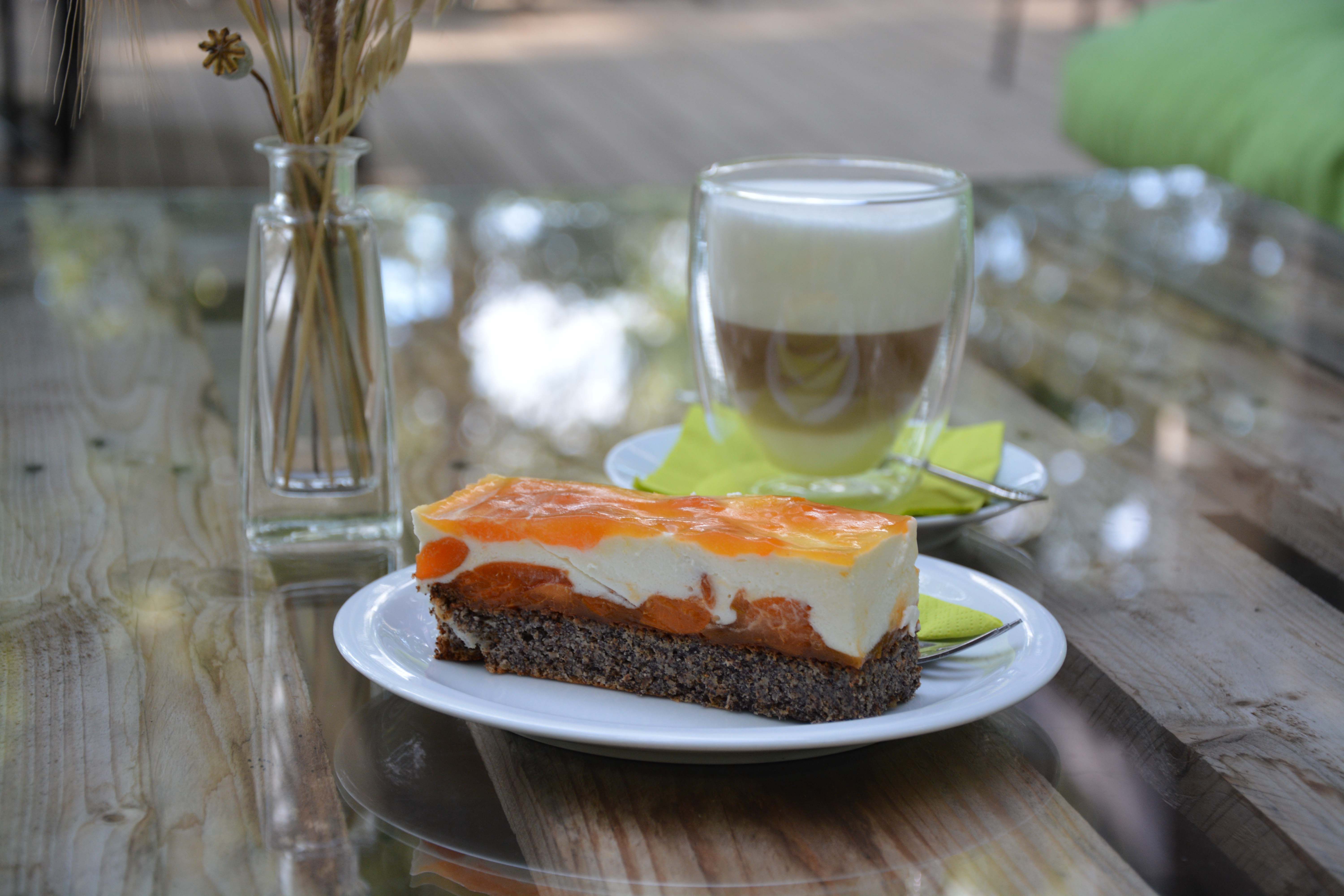 Tányér gyümölcstortával a faasztalon, a háttérben egy pohár kávéval és egy váza.