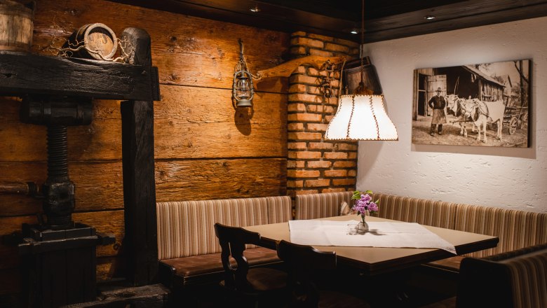 Hangulatos szalon, fából készült falakkal, sarokpaddal, virágos asztallal és lámpával. A falon történelmi fénykép lóg.