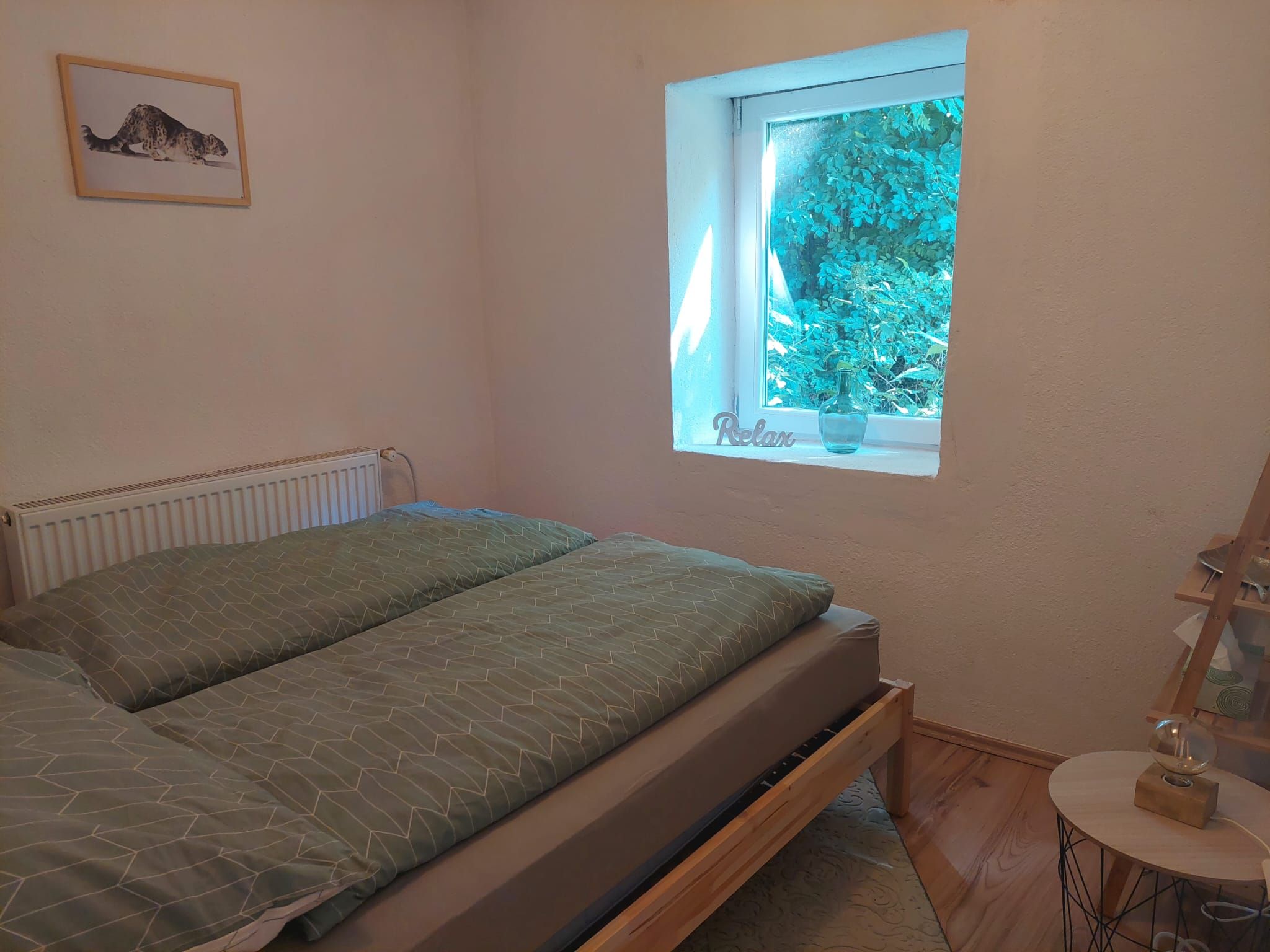 Hangulatos hálószoba egy ággyal, egy ablakkal, ahonnan kilátás nyílik a zöldre, és egy képpel a falon.