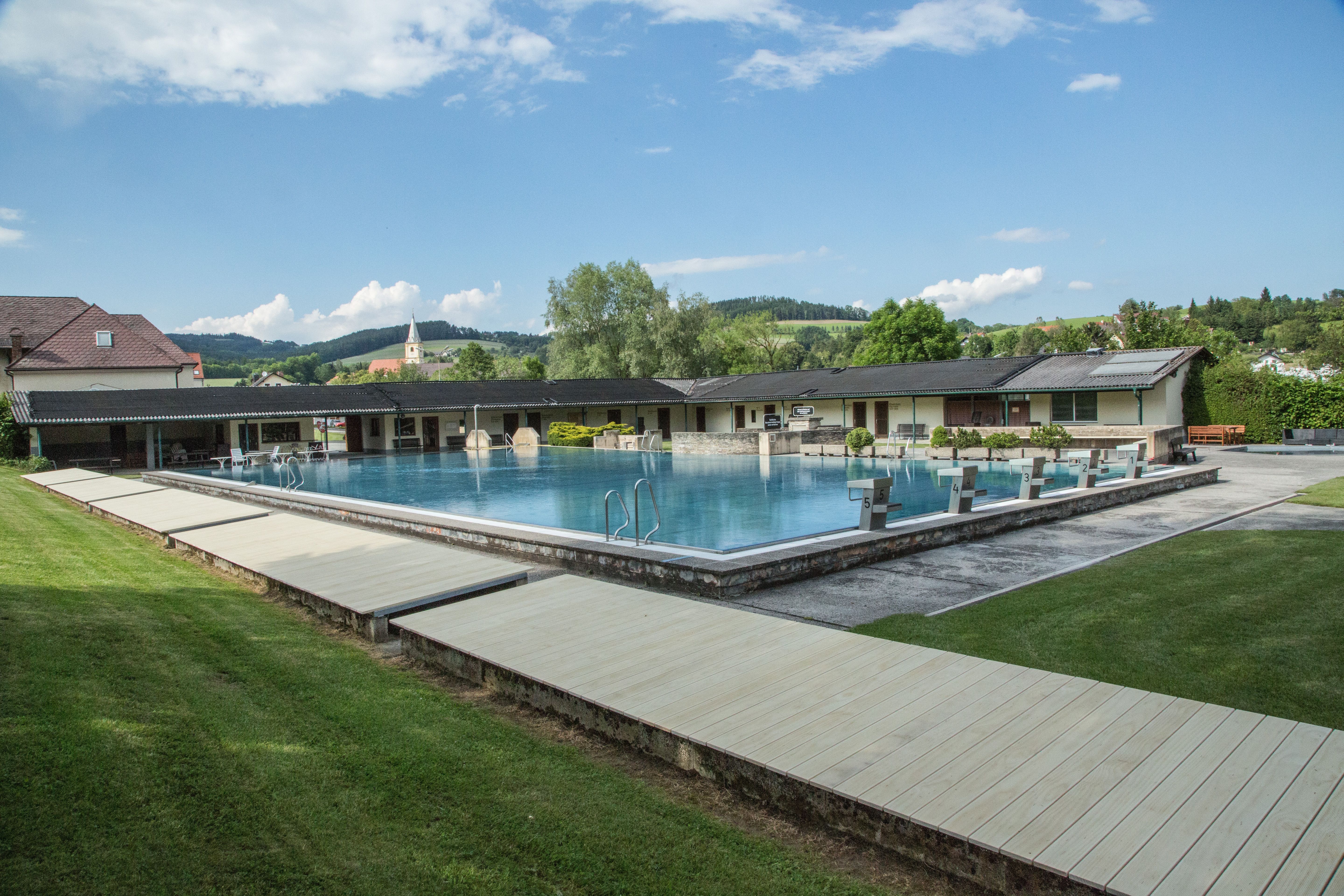 Krumbach szabadtéri medence úszómedencével és búvárblokkokkal, zöld tájjal és épületekkel körülvéve.