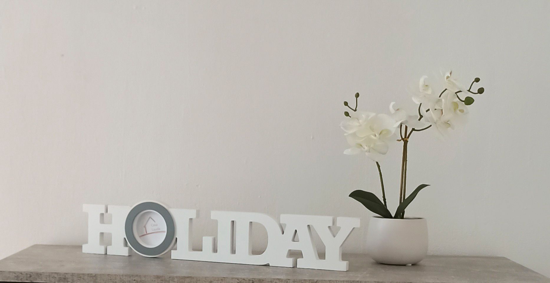 Dekoráció 'HOLIDAY' felirattal és fehér orchideával egy cserépben egy asztalon.