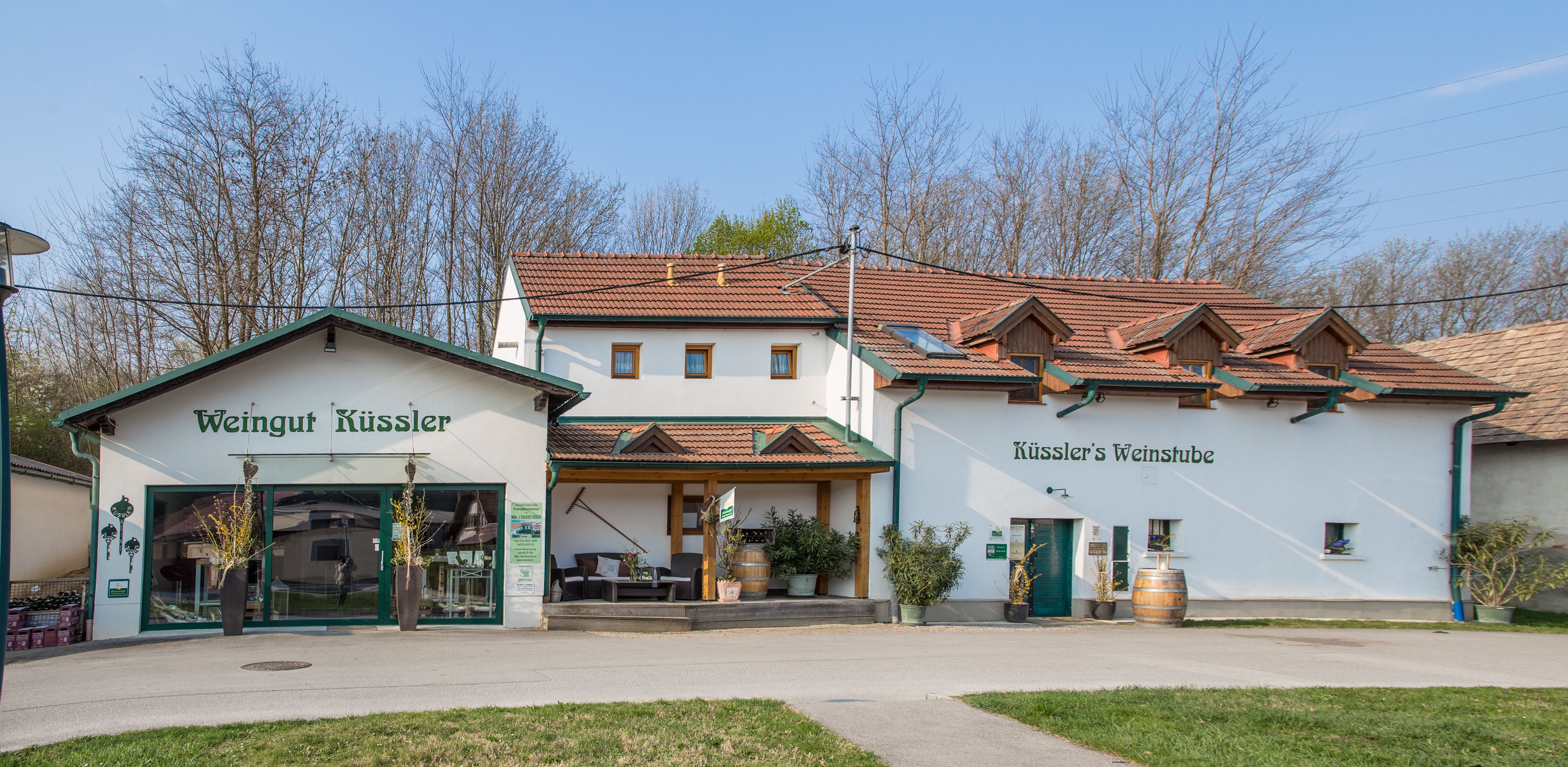 Weingut Küssler borbárral és terasszal, fákkal körülvéve.