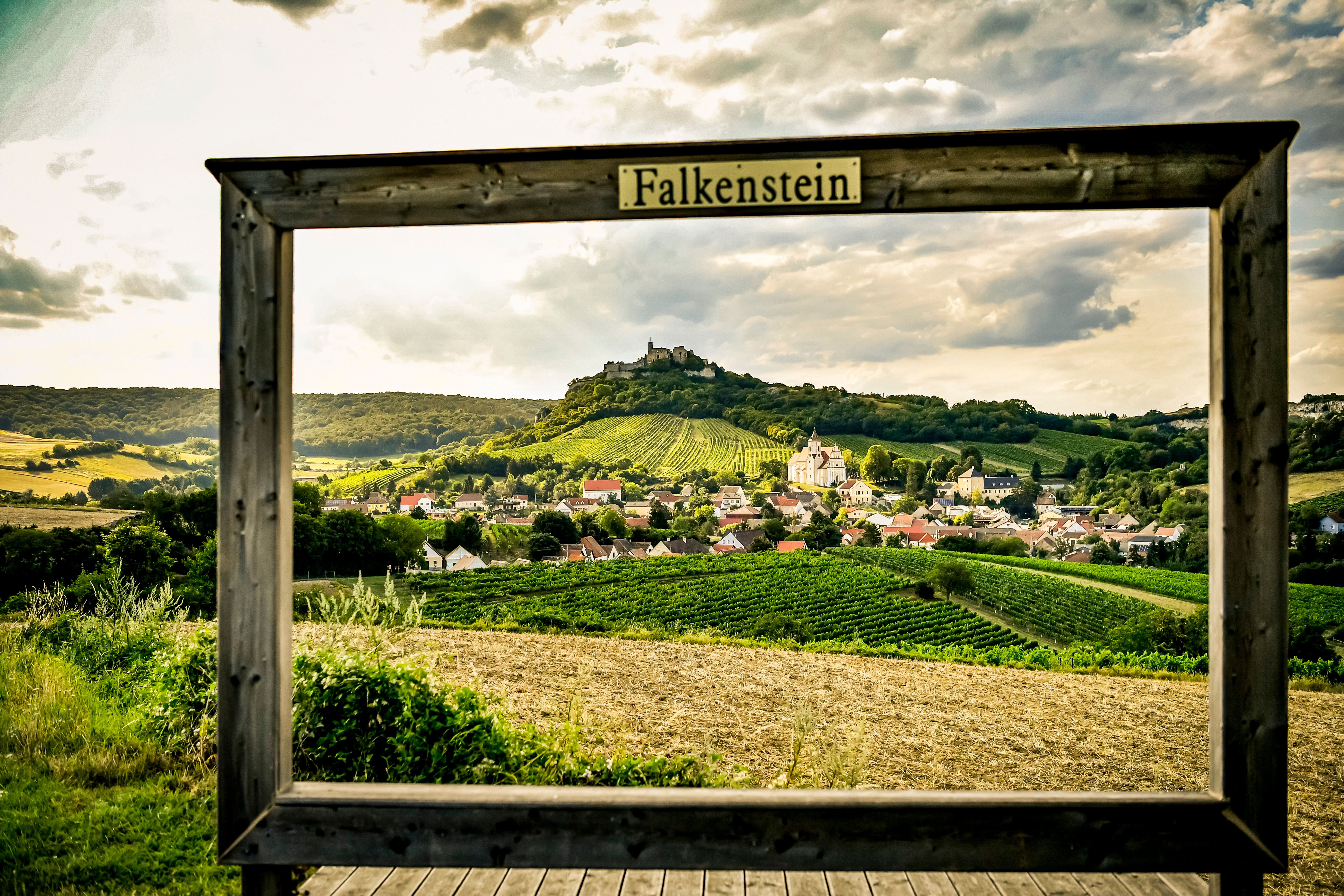 Falkenstein falu látképe, a háttérben szőlőültetvényekkel és egy romos várral, fakeretben "Falkenstein" felirattal.
