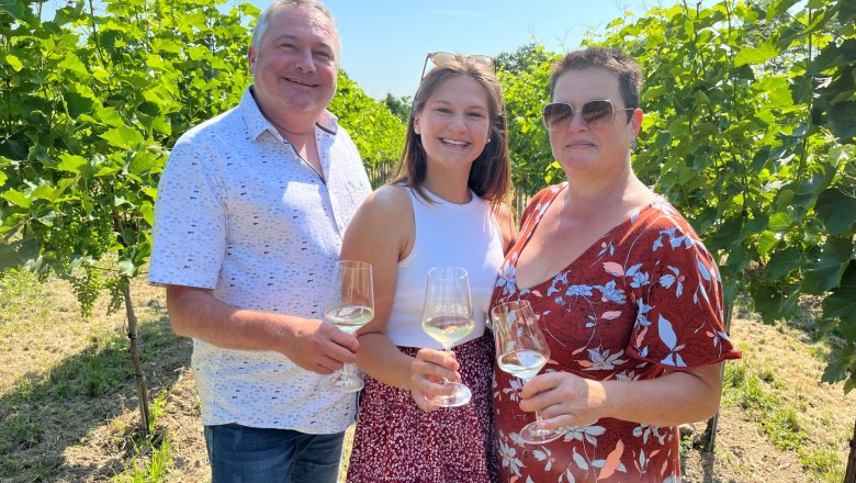 A Heimel csal&aacute;d borospoharakkal a kez&eacute;ben. A csal&aacute;d a szőlőtők&eacute;k k&ouml;z&ouml;tt &aacute;ll.