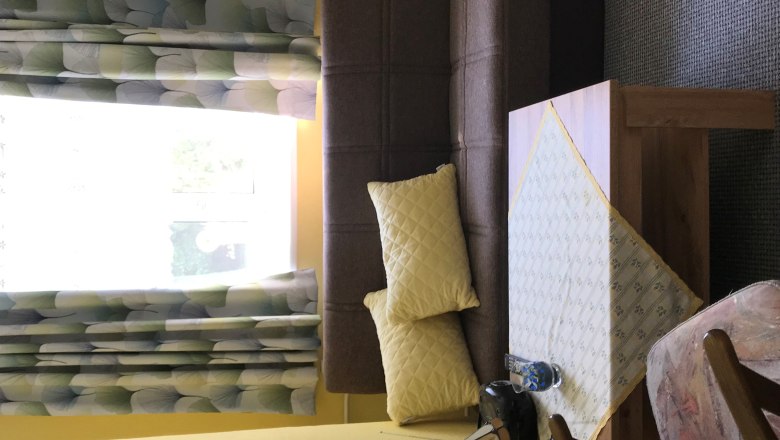 Nappali barna kanap&eacute;val, s&aacute;rga p&aacute;rn&aacute;kkal, asztallal ter&iacute;tővel, fotel &eacute;s ablak mint&aacute;s f&uuml;gg&ouml;nnyel.