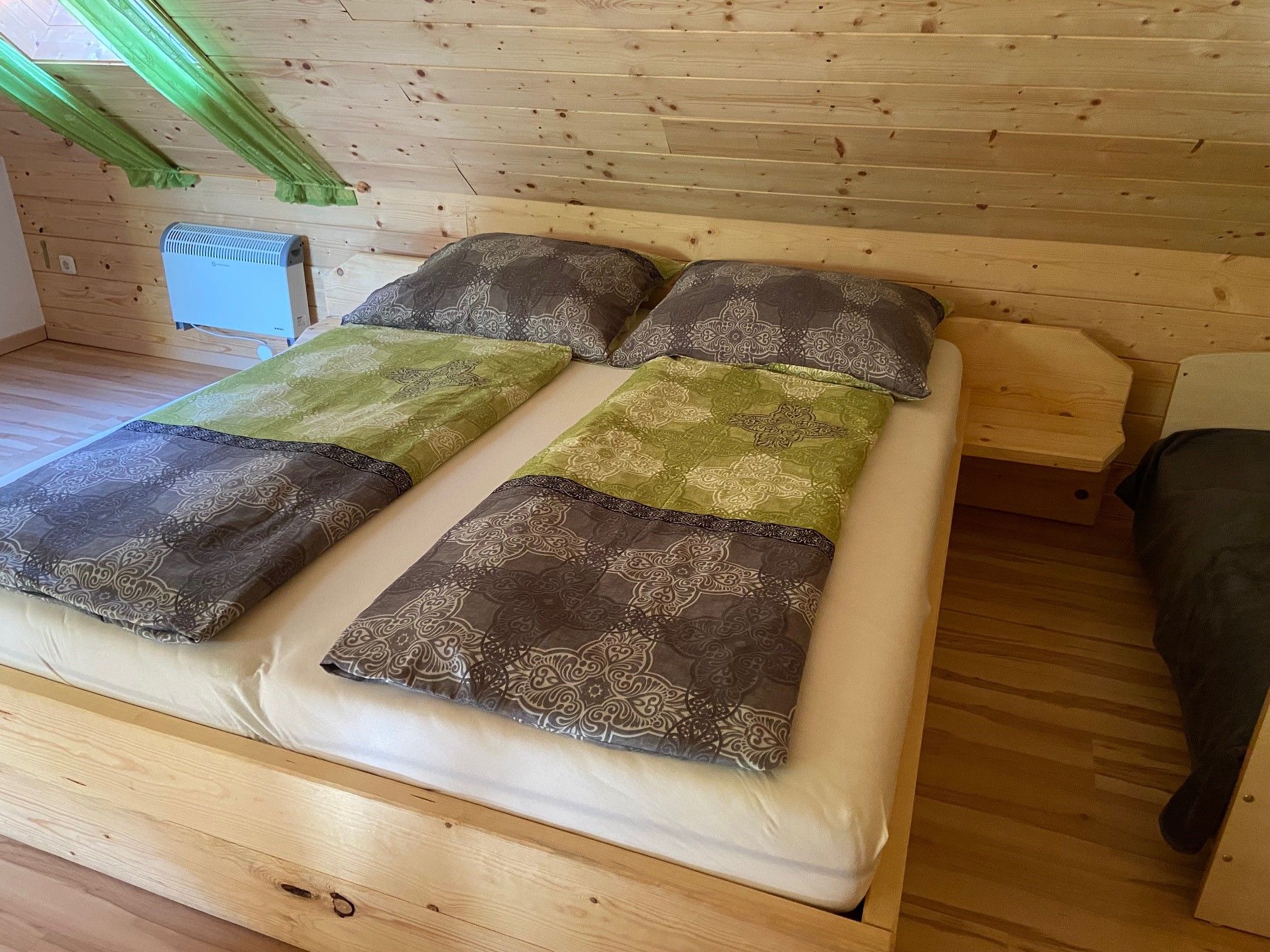 Kétágyas ágy egy faburkolatos szobában, zöld függönyökkel.