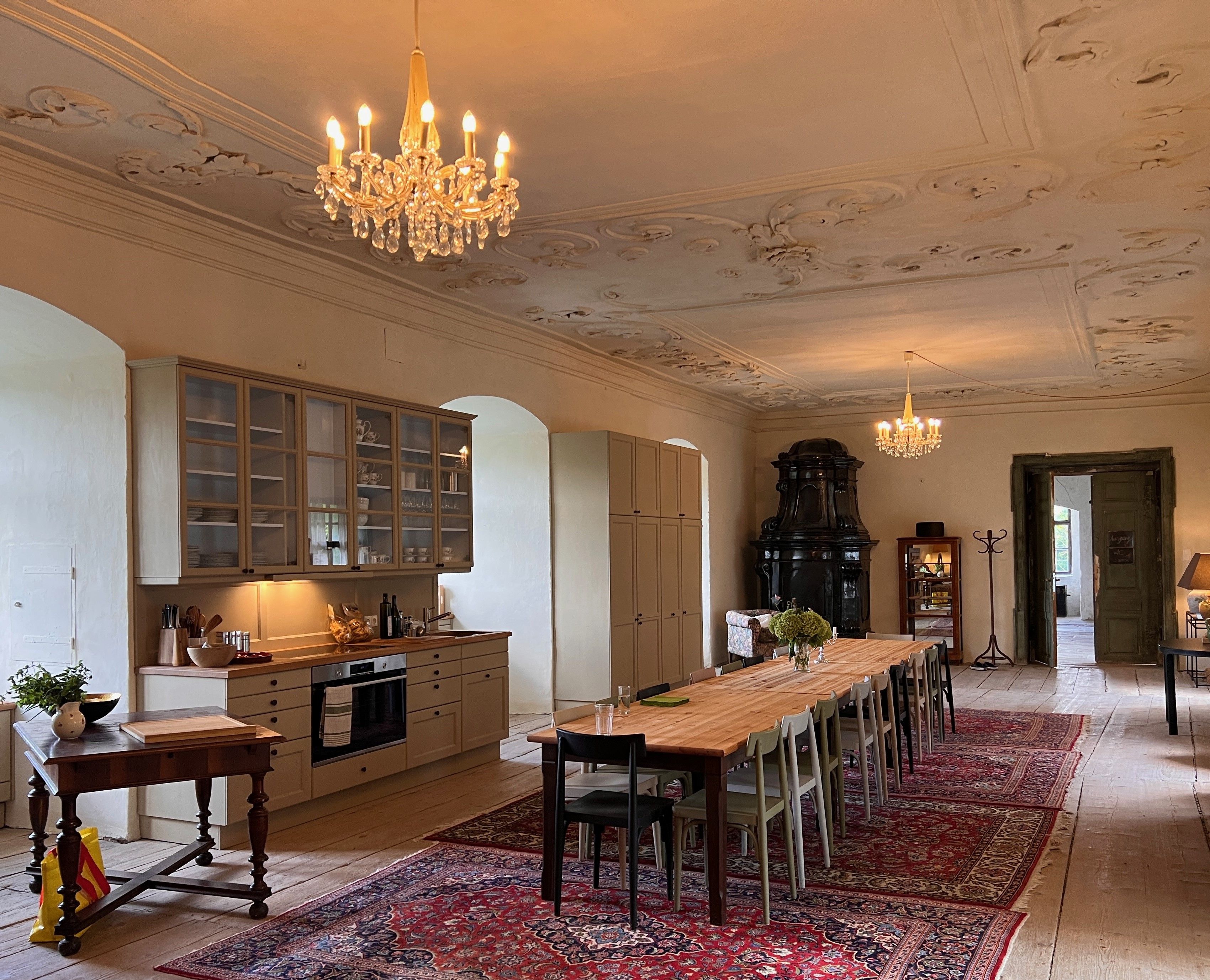 Elegáns étkező hosszú faasztallal, csillárokkal és antik kályhával.
