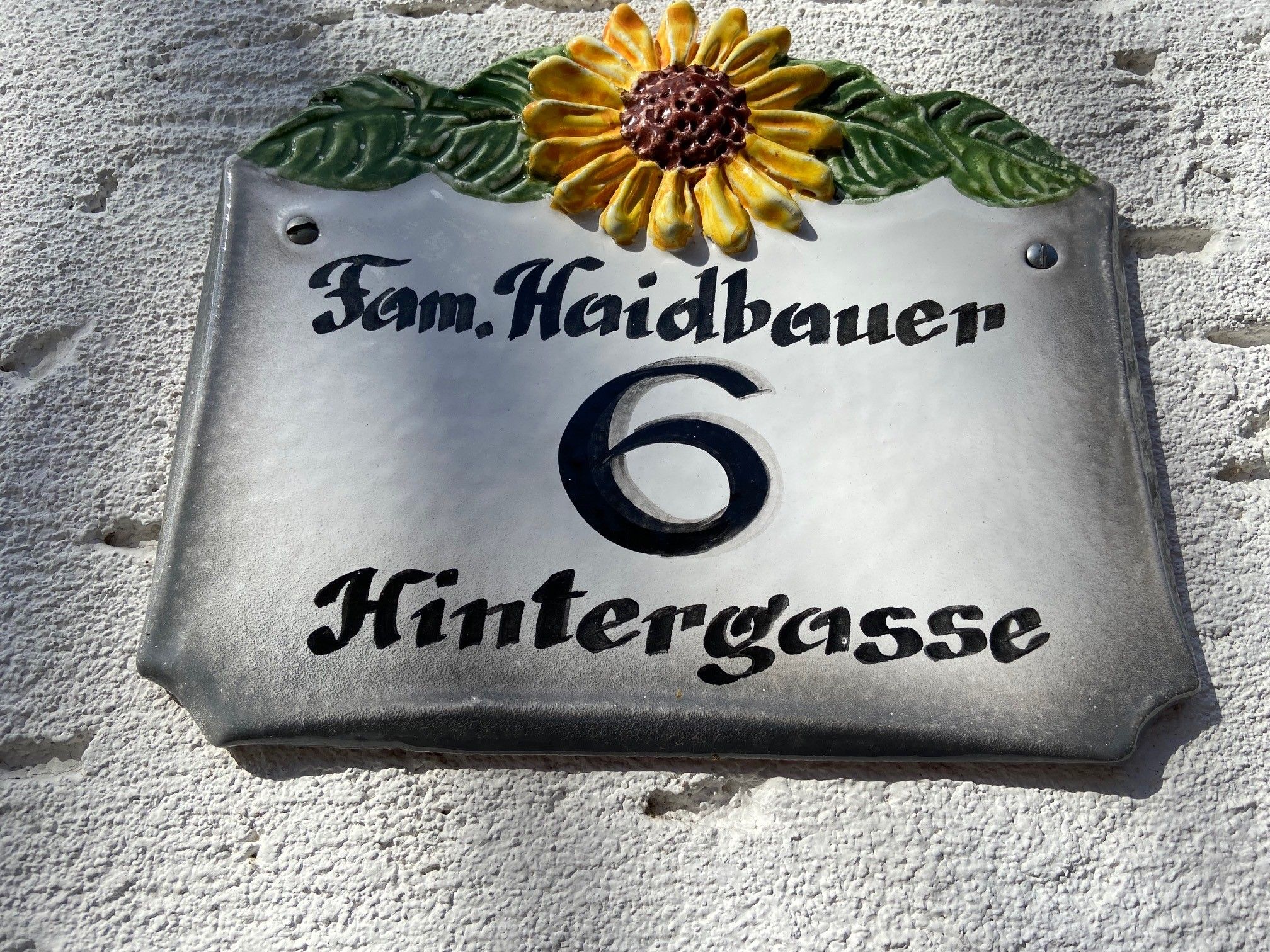 Házszámtábla napraforgóval és a "Fam. Haidbauer 6 Hintergasse" felirattal.
