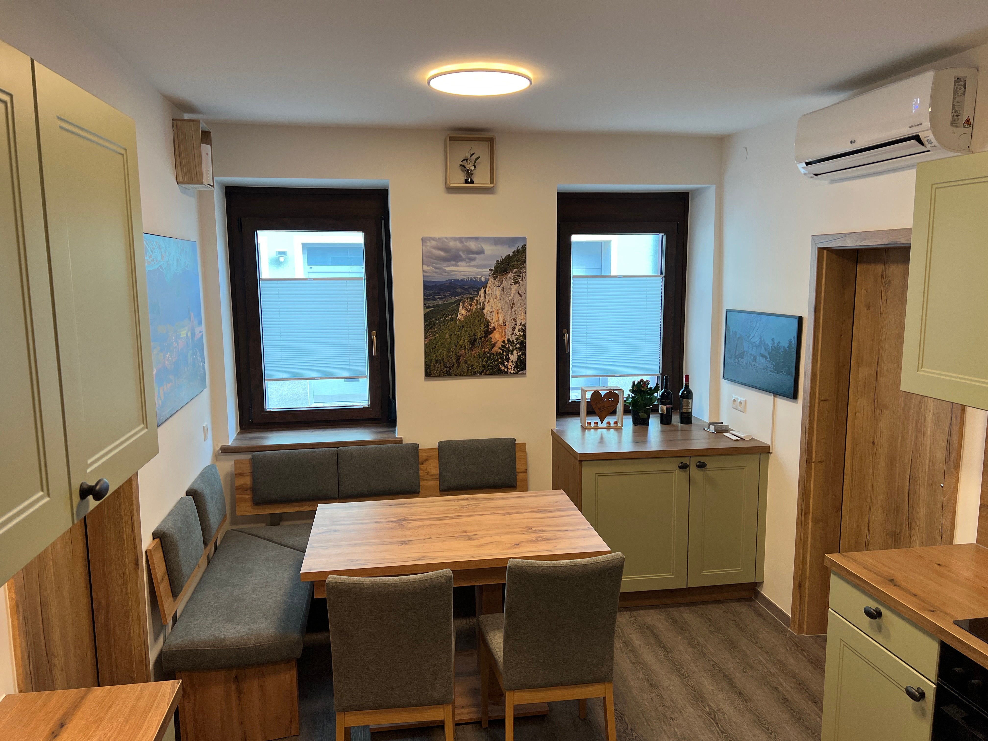 Modern konyha fabútorokkal, étkezőasztallal és zöld szekrényekkel.