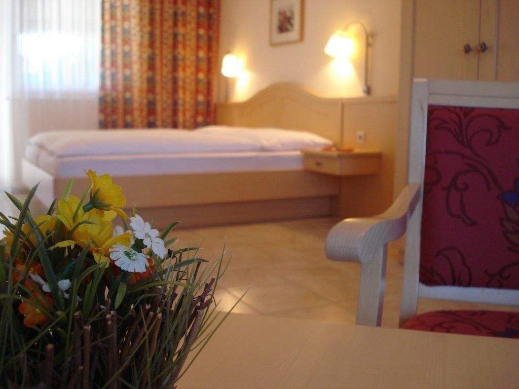 Hangulatos vendégszoba egy ággyal, egy székkel és egy virágos asztallal.