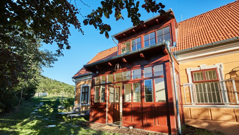 Sárga villa piros tetőcseréppel és üvegezett bejárattal, fákkal és zöld kerttel körülvéve.