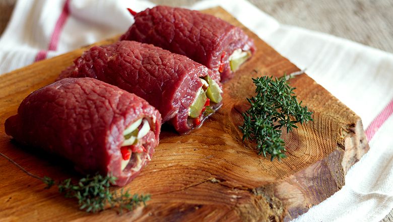 Három töltött nyers marhahúsroulád fadeszkán, kakukkfűágakkal.