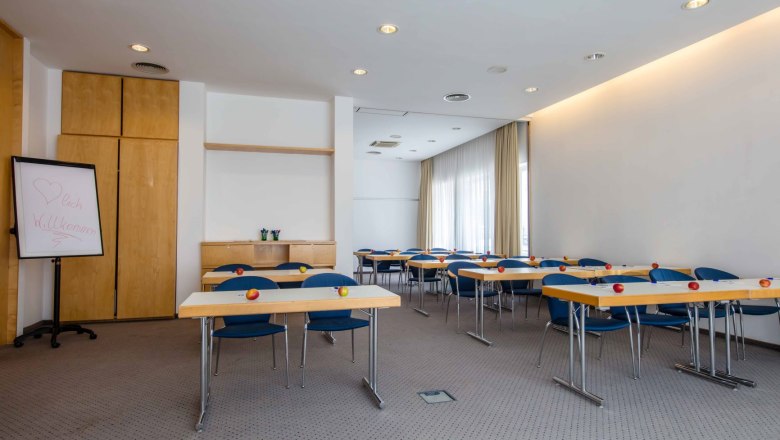 Egy szemin&aacute;riumi terem asztalokkal, sz&eacute;kekkel &eacute;s alm&aacute;kkal az asztalokon.