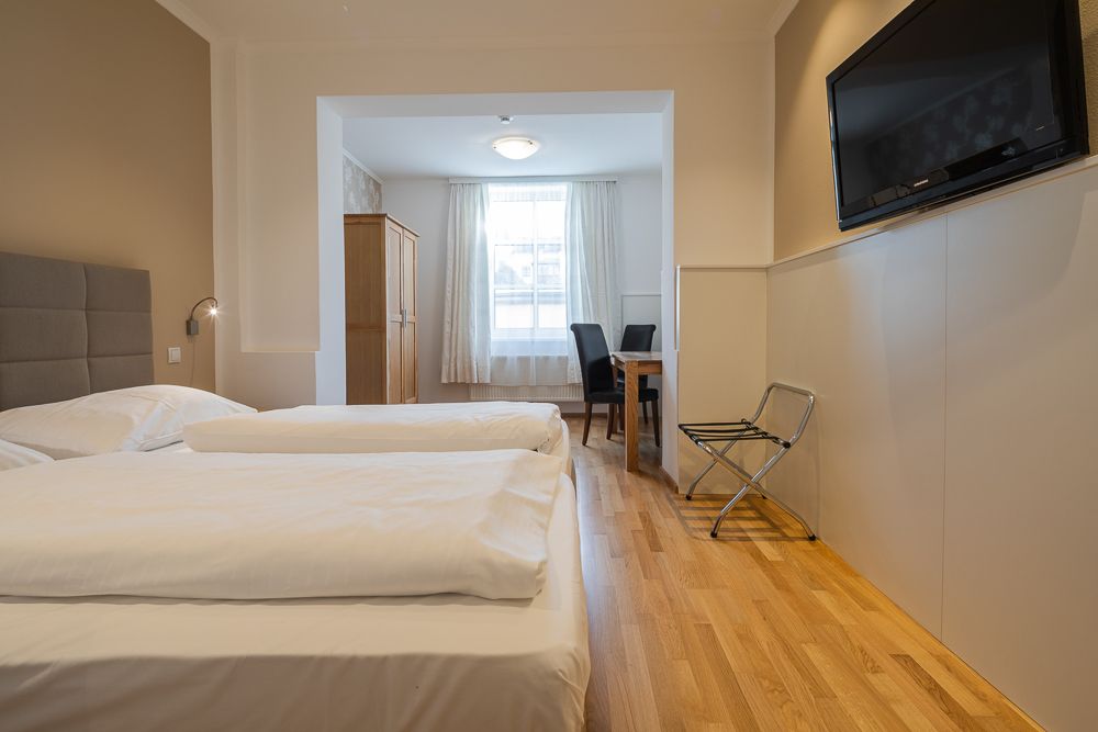 Hotelszoba két ággyal, televízióval, asztallal és székekkel.