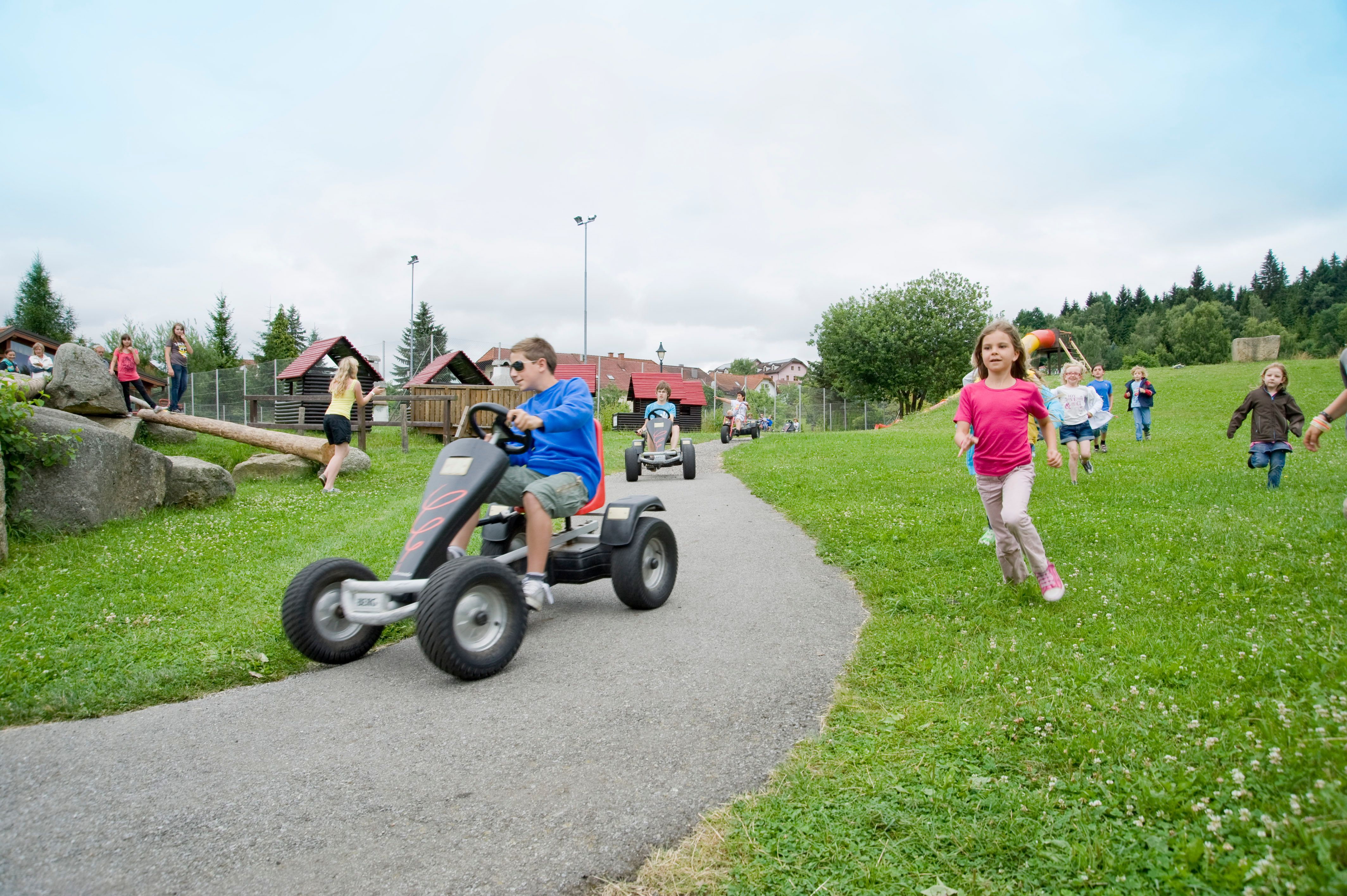 A gyerekek játszanak a Kettcars kalandjátszótéren, és futnak a réten.