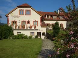 Nagy, hagyományos ház, vörös tetővel és virágos kerttel az előtérben.