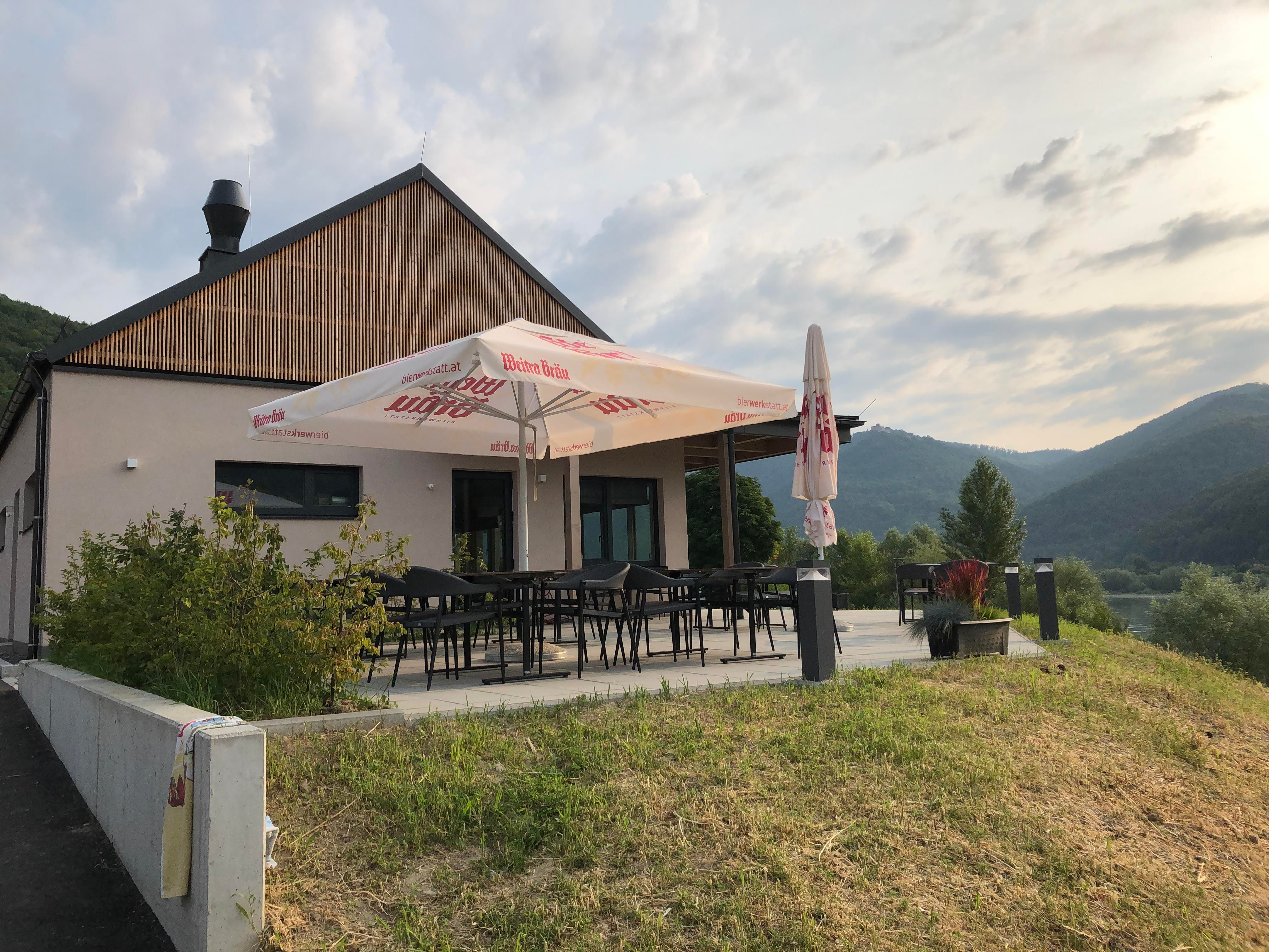 Modern terasz napernyővel, zöld vidékkel és dombokkal körülvéve.