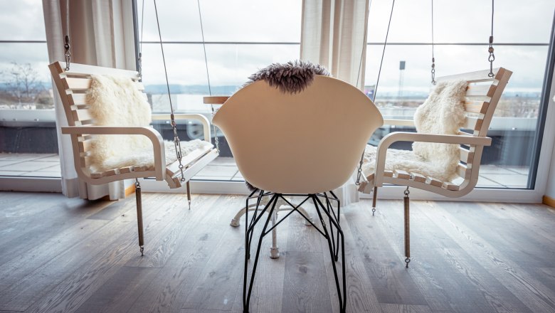 Belső t&eacute;r hintasz&eacute;kekkel &eacute;s egy modern sz&eacute;kkel a nagy ablakok előtt.