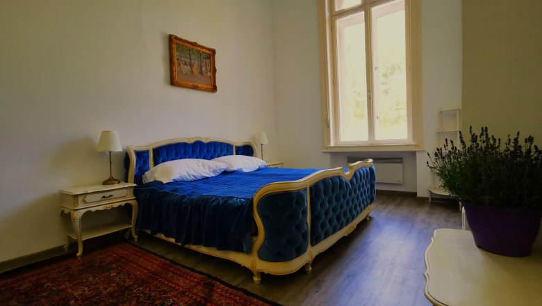 Eleg&aacute;ns h&aacute;l&oacute;szoba k&eacute;k &aacute;ggyal, antik b&uacute;torokkal &eacute;s nagy ablakkal.