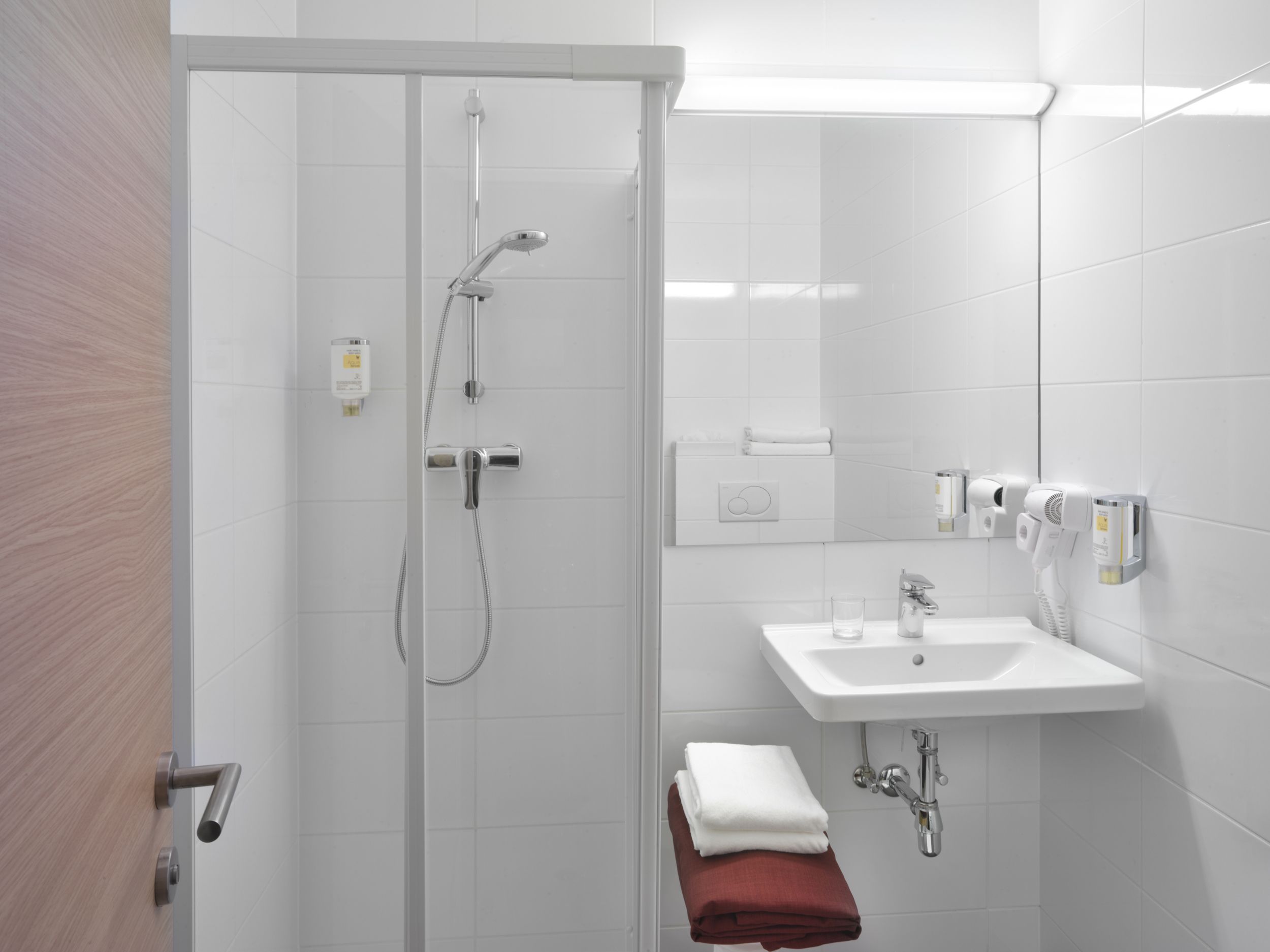 Modern szállodai fürdőszoba zuhanyzóval, mosdókagylóval és törölközőkkel.
