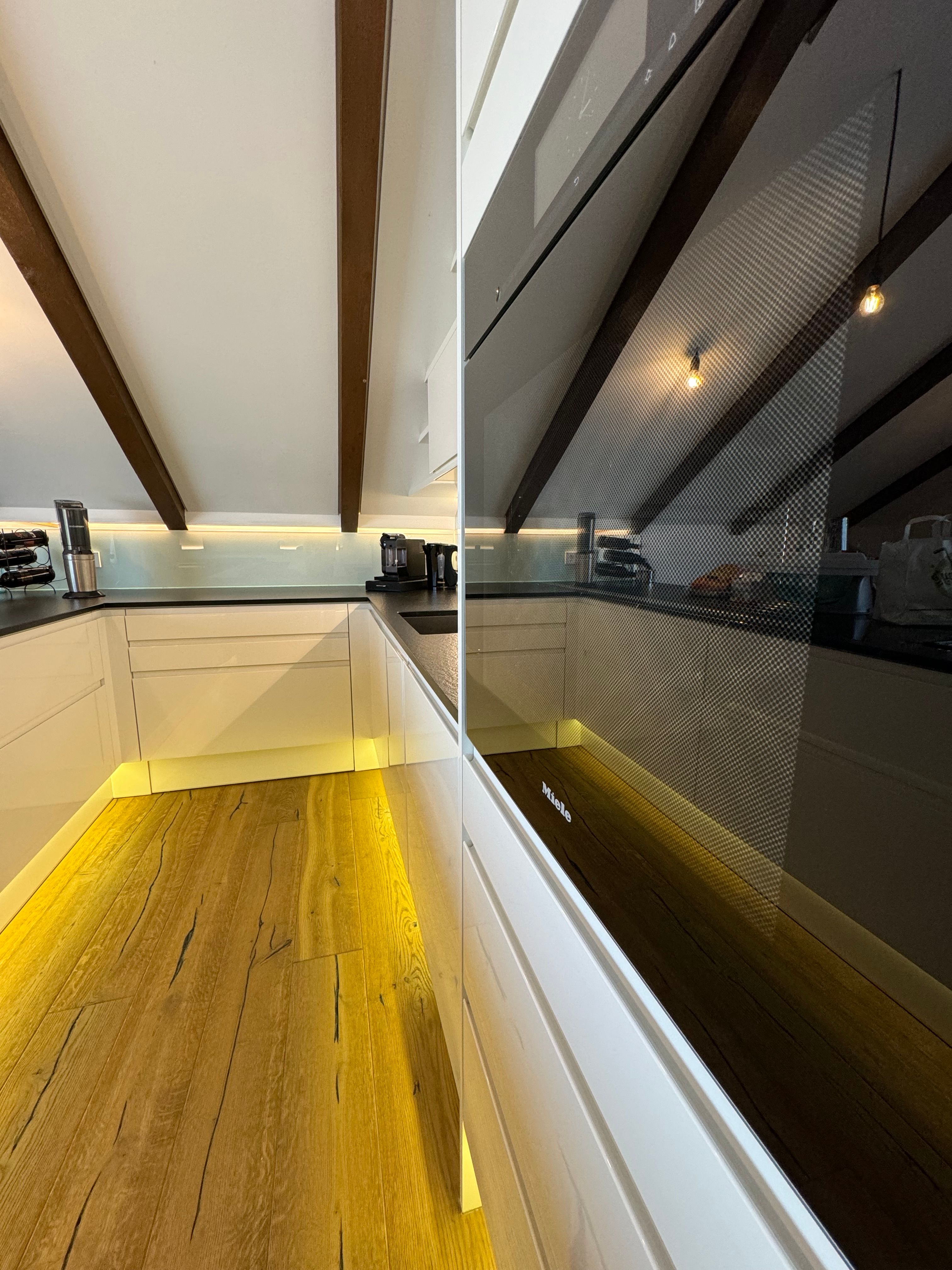 Modern konyha fapadlóval, fehér szekrényekkel és beépített sütővel.