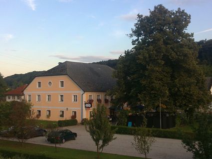 Kilátás egy sárga vendéglőre egy nagy fával és parkolóval.