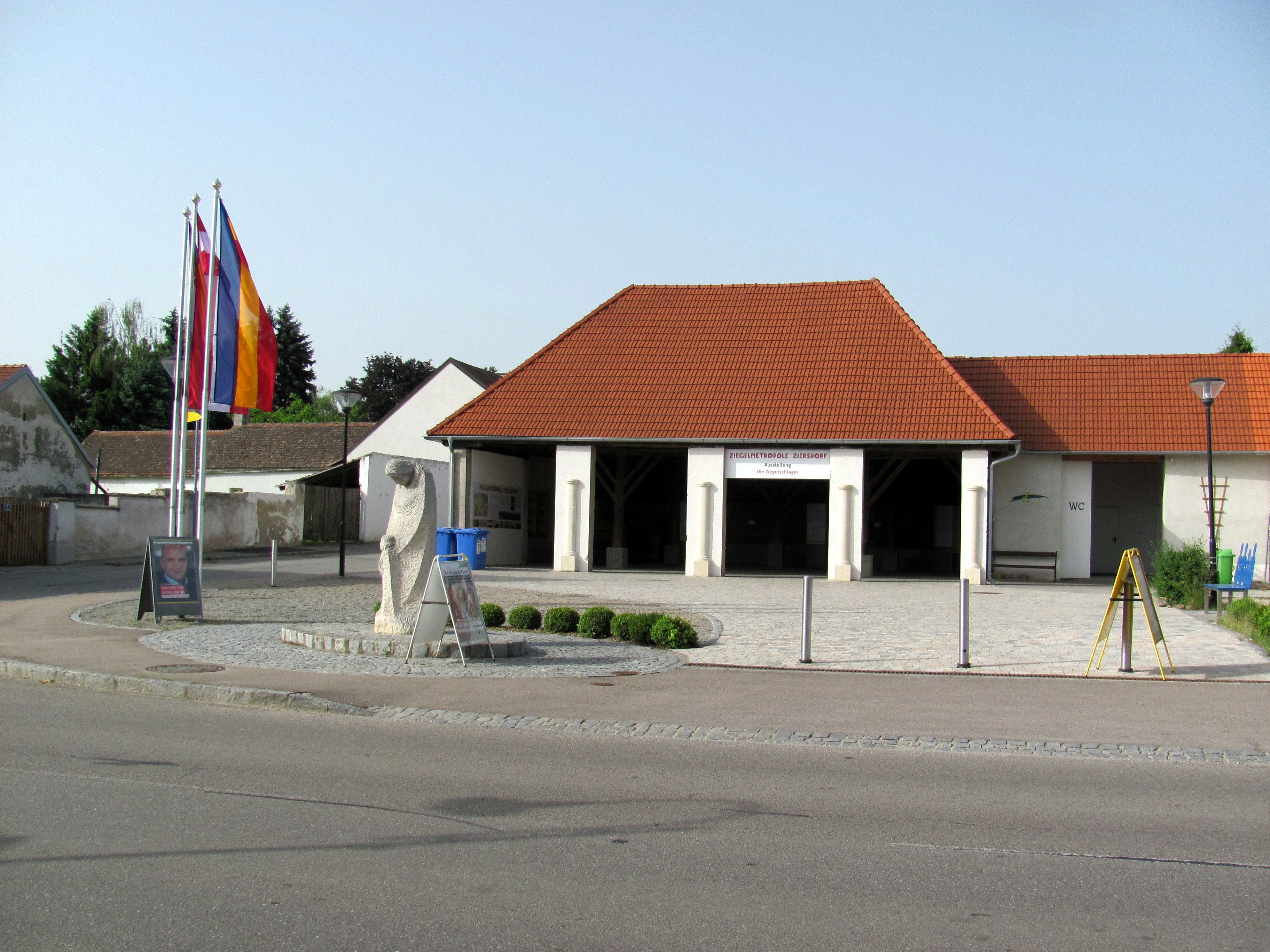 A ziersdorfi téglamúzeum külső nézete vörös tetőcserepekkel és zászlókkal.